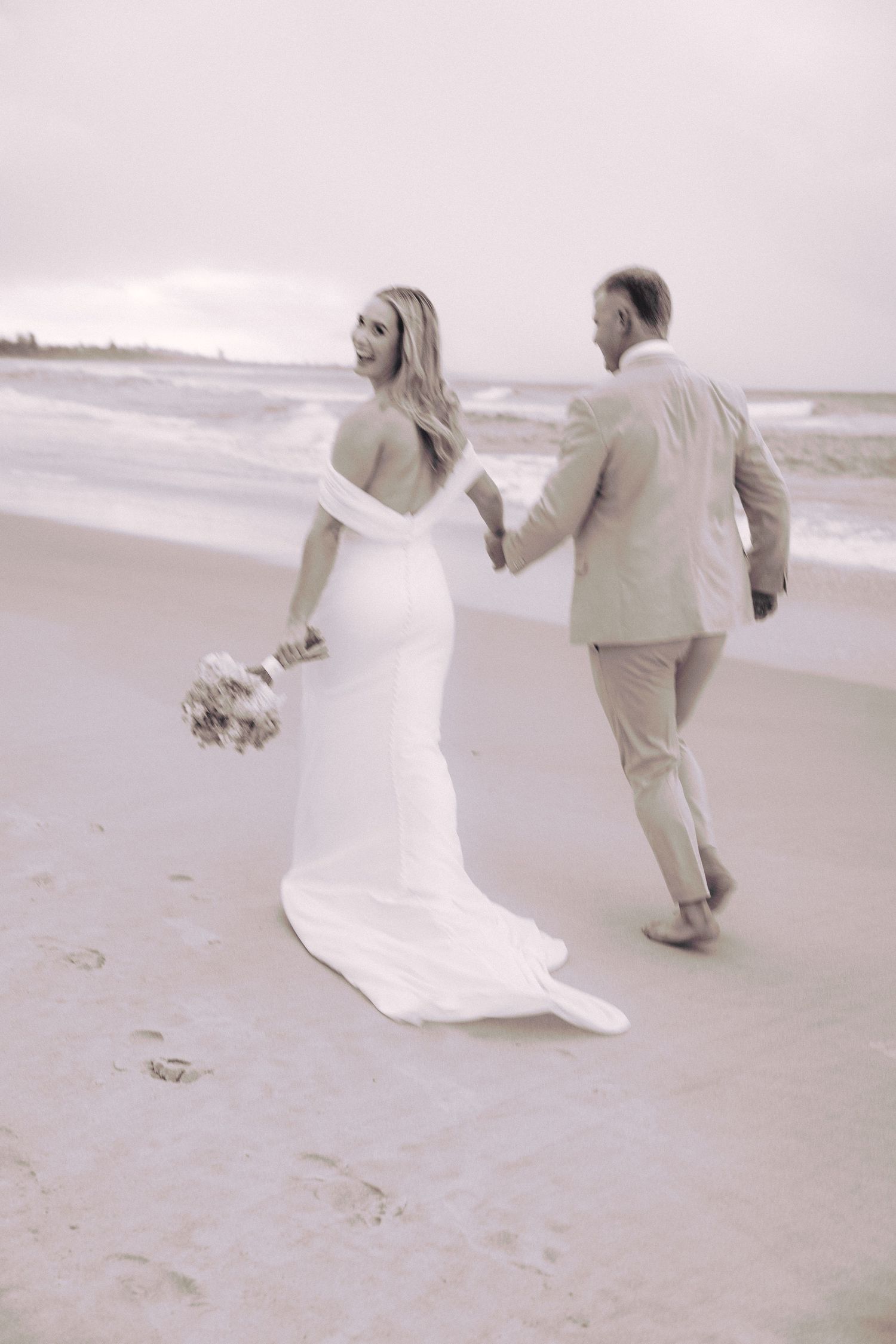 Black and white wedding portrait of the bride and groom running along the beach with artistic motion blur.
