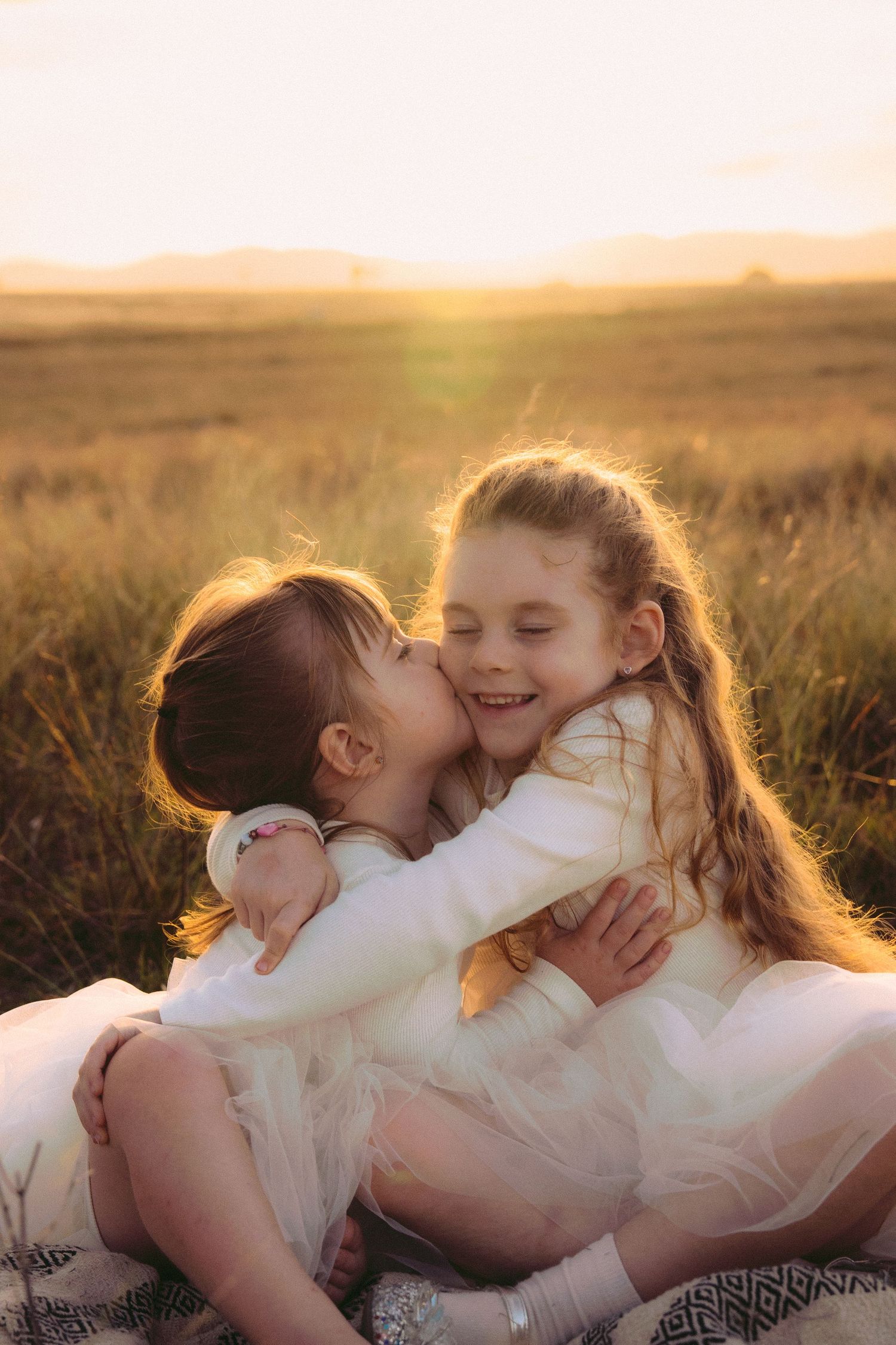 Sisters cuddling behind warm golden sun during their family session