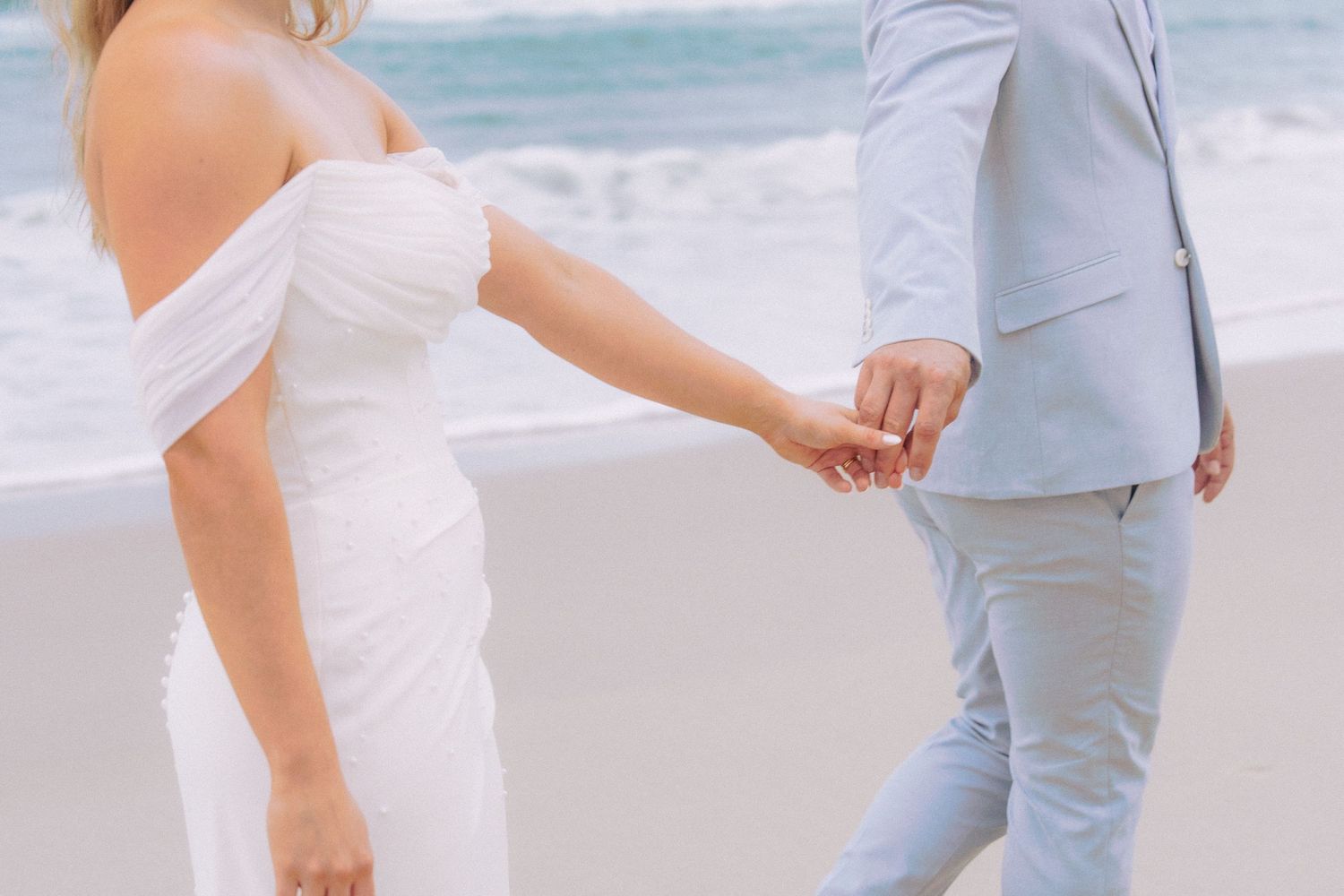 Bride and groom holding hands while walking along the beach after their wedding ceremony.