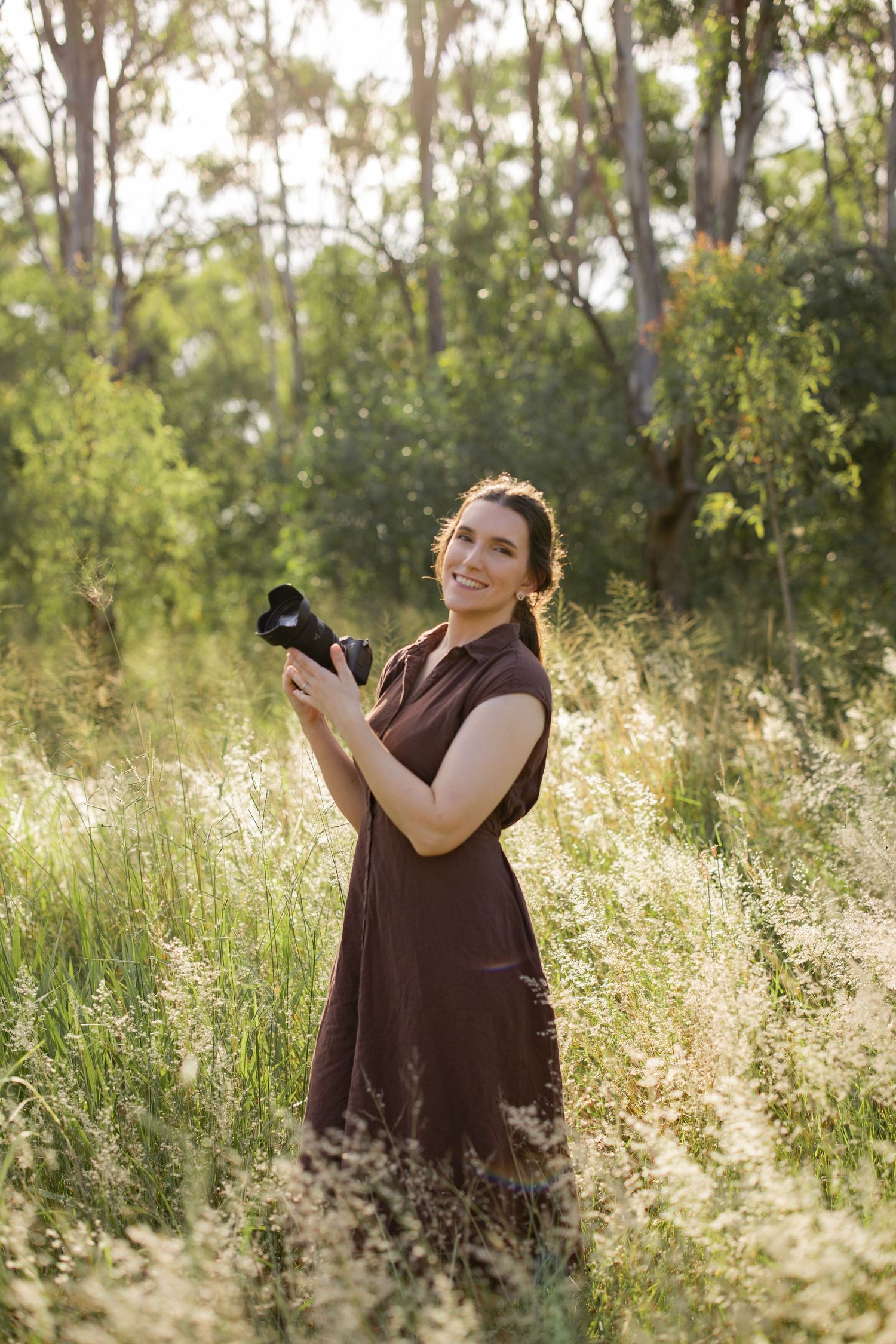 Portrait of photographer Teyah Rose holding a camera and smiling outdoors.