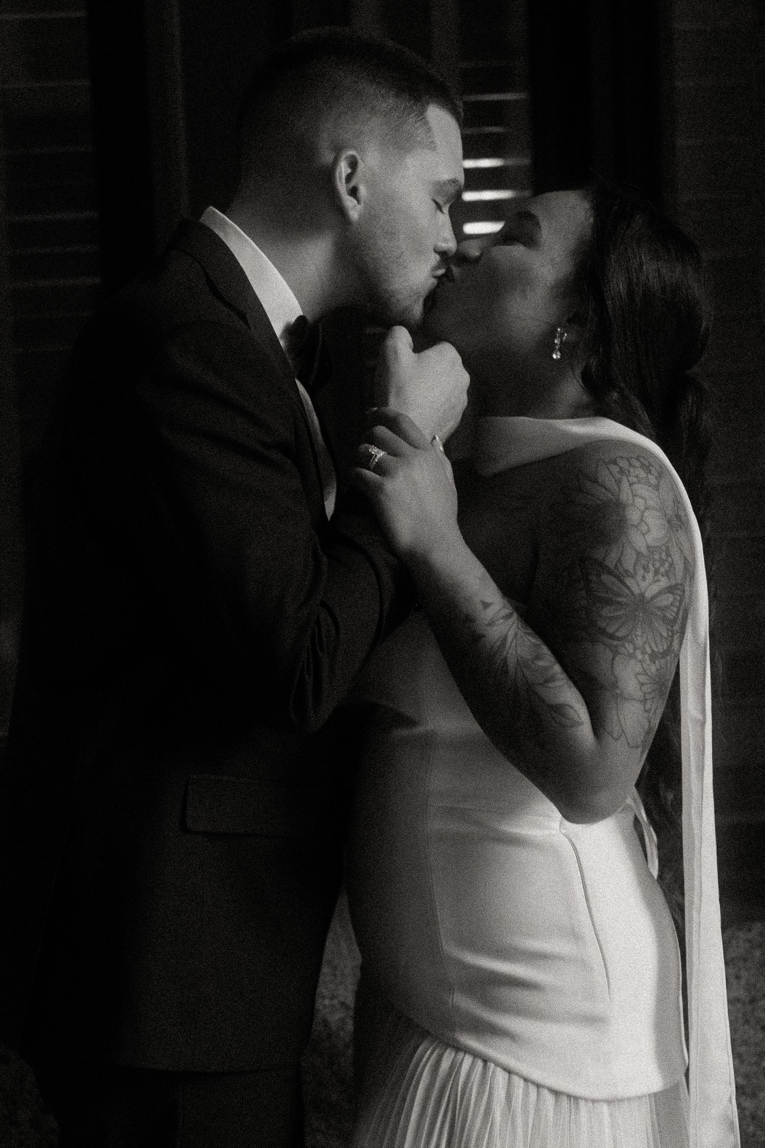 Black and white photo of tattooed bride and groom sharing a kiss on their wedding day.