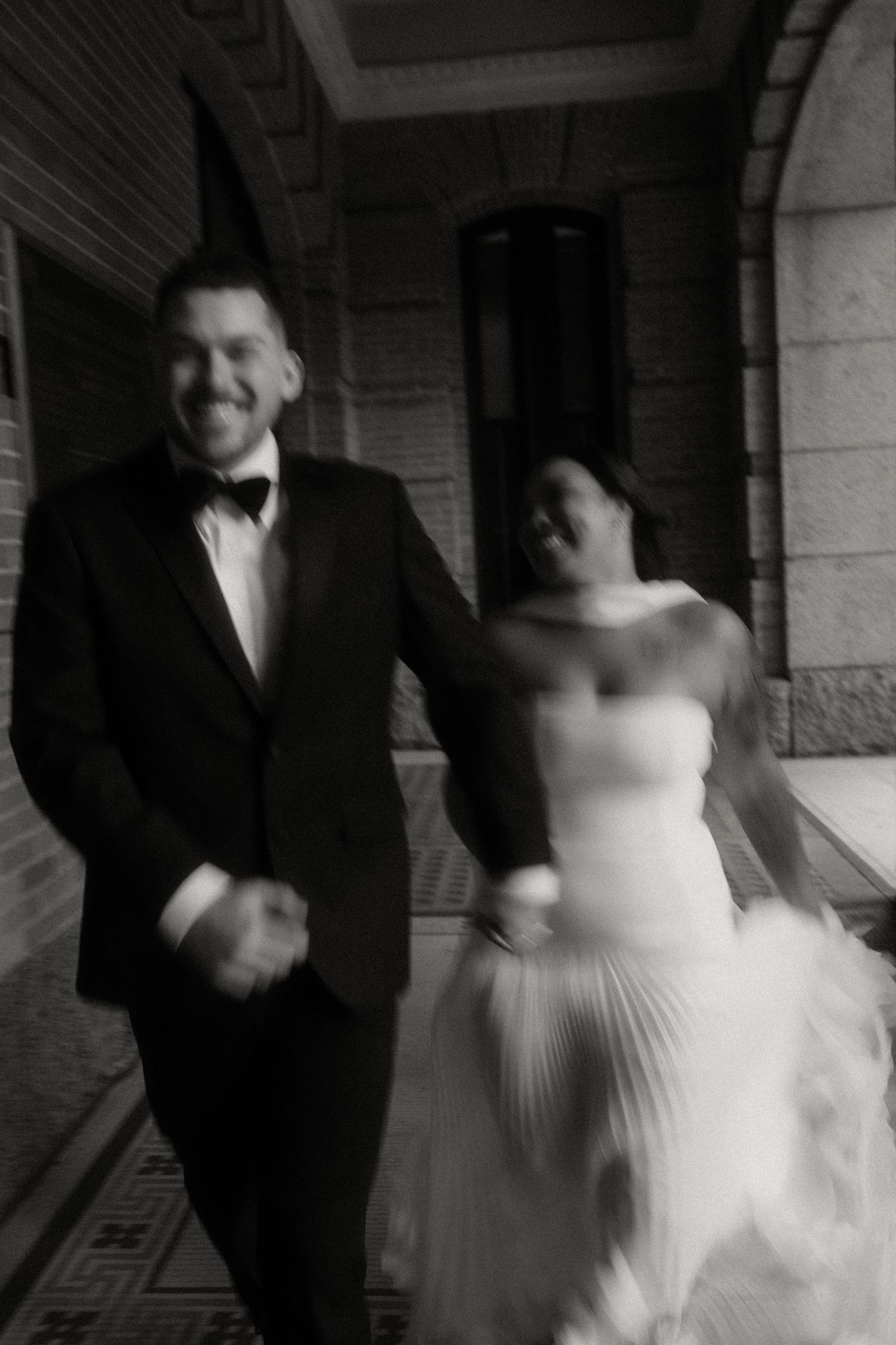 Joyful black and white motion blur photo of bride and groom running and laughing together.