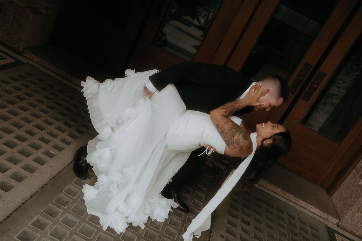Groom dramatically dips and kisses bride in flowing white gown on ornate tiled floor.