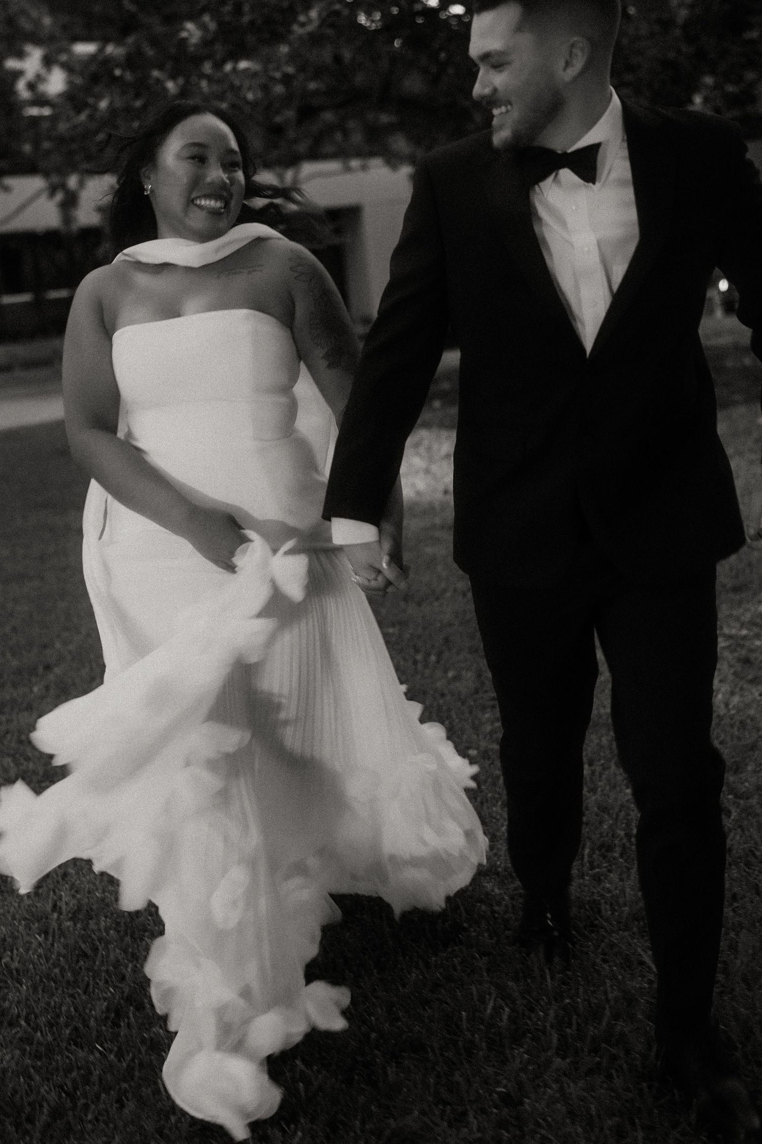 Black and white photo of smiling bride and groom walking hand in hand on their wedding day.