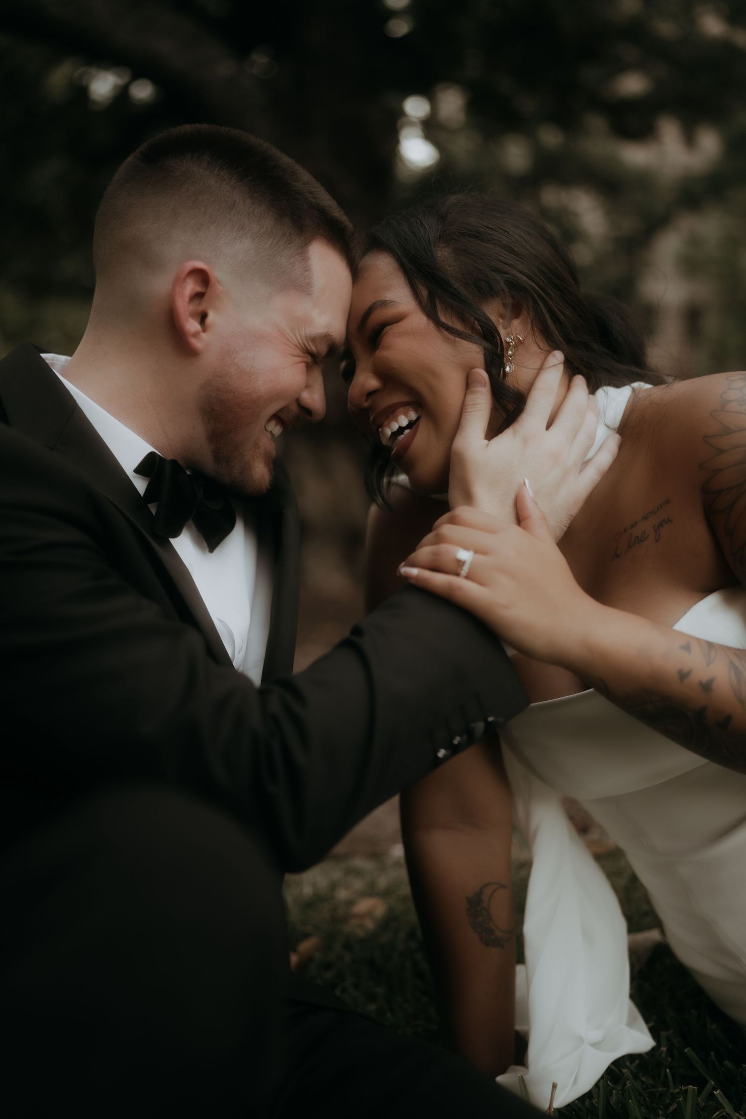 Joyful bride and groom laugh together forehead-to-forehead during outdoor wedding portraits.