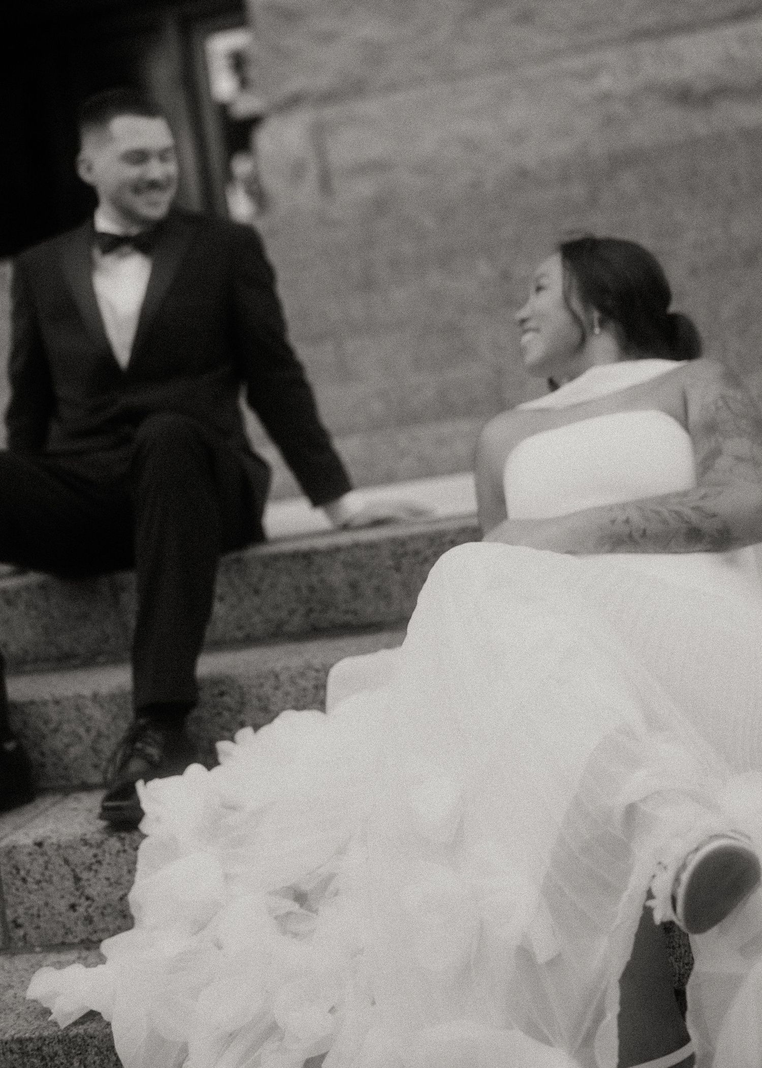 Black and white photo of smiling bride and groom sitting on stone steps together.