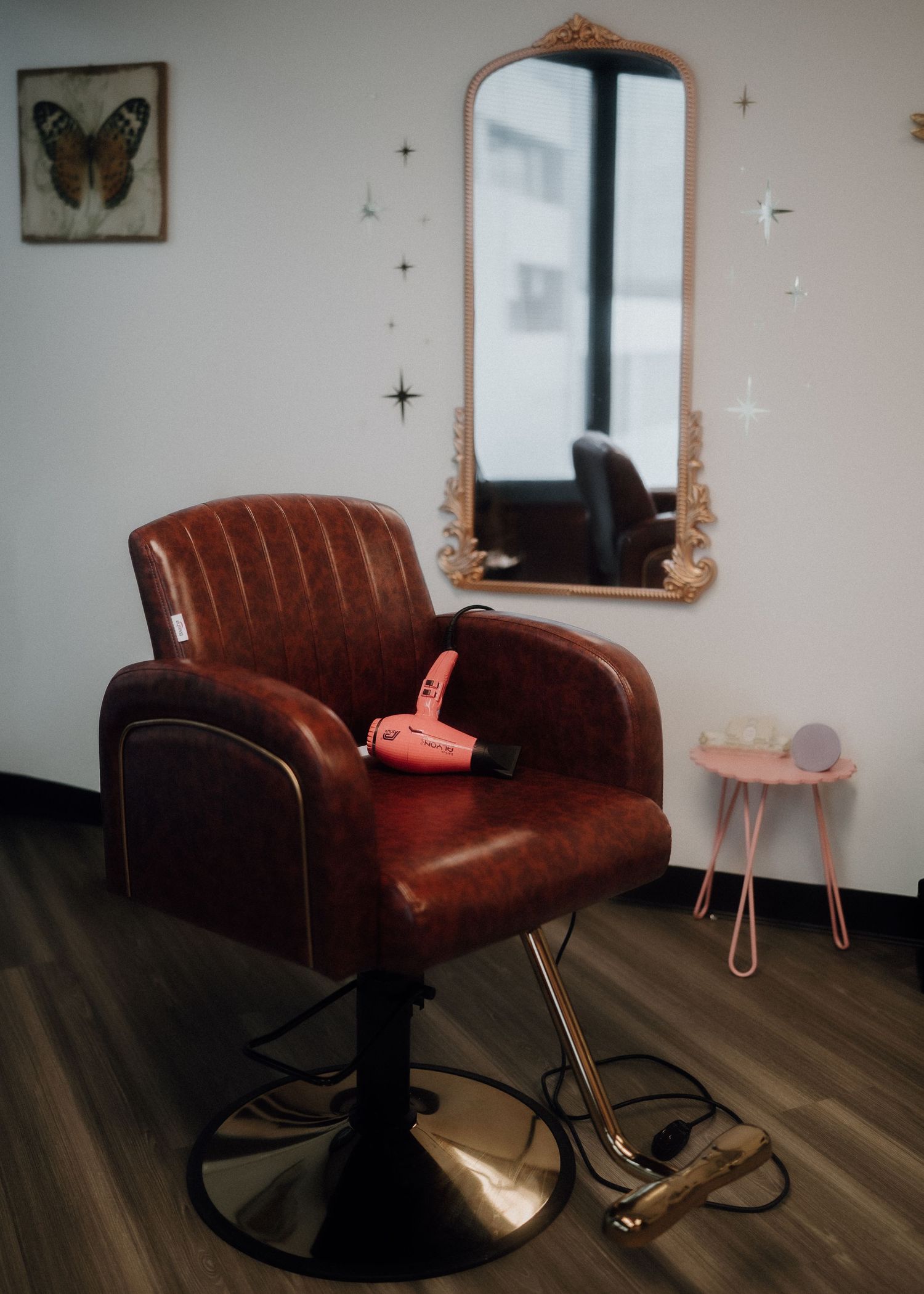 Brown leather salon chair with pink hair dryer, gold mirror, and star wall decor in a stylish hair salon.