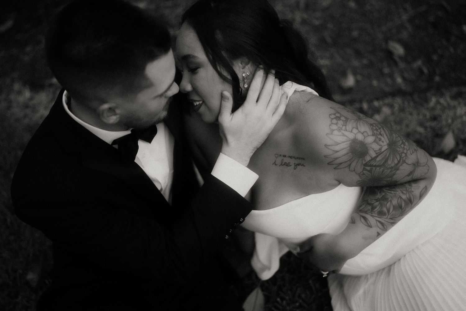 Black and white photo of tattooed bride and groom sharing an intimate moment outdoors on their wedding day.