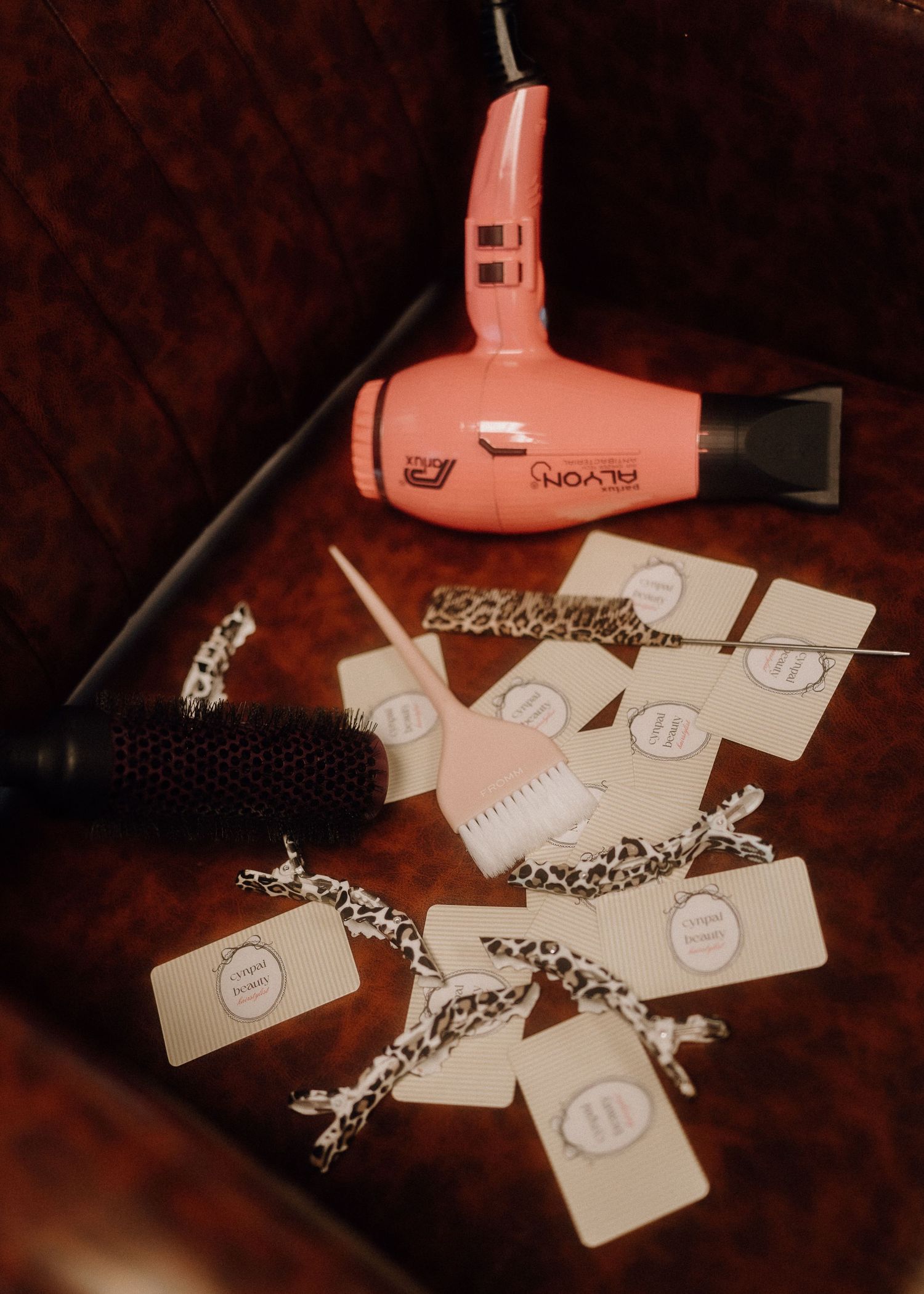Pink Parlyon hair dryer with round brush, comb, and gift tags with leopard print ribbons on brown leather.