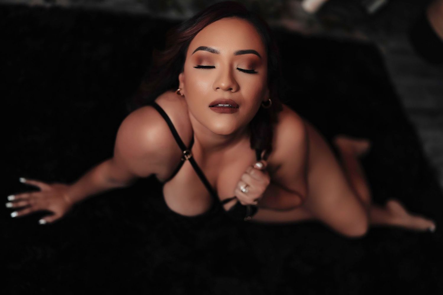 Woman in black lingerie posing on dark fur background in artistic boudoir photography.