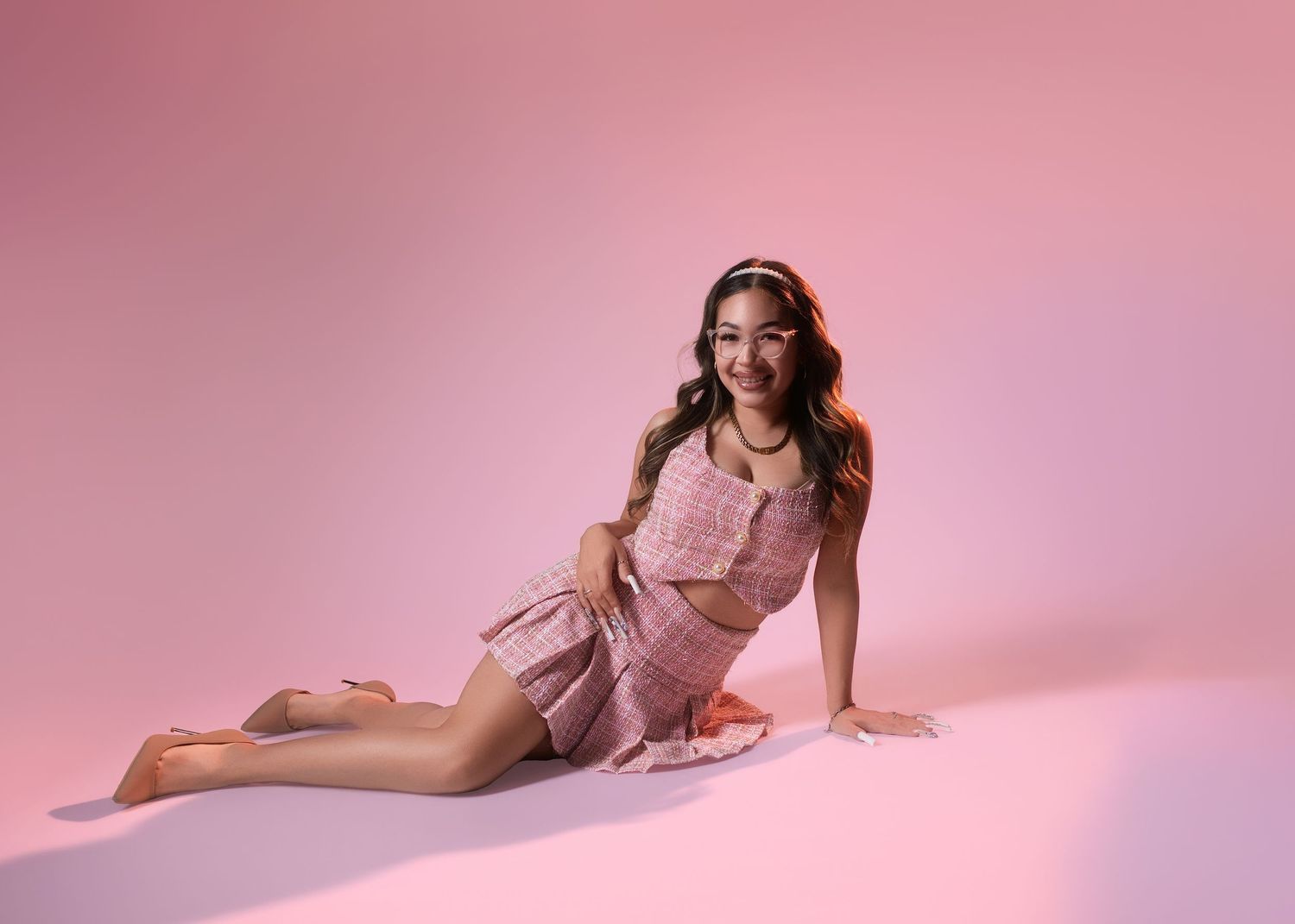 Young woman in a pink outfit sitting gracefully against a soft pink studio background.