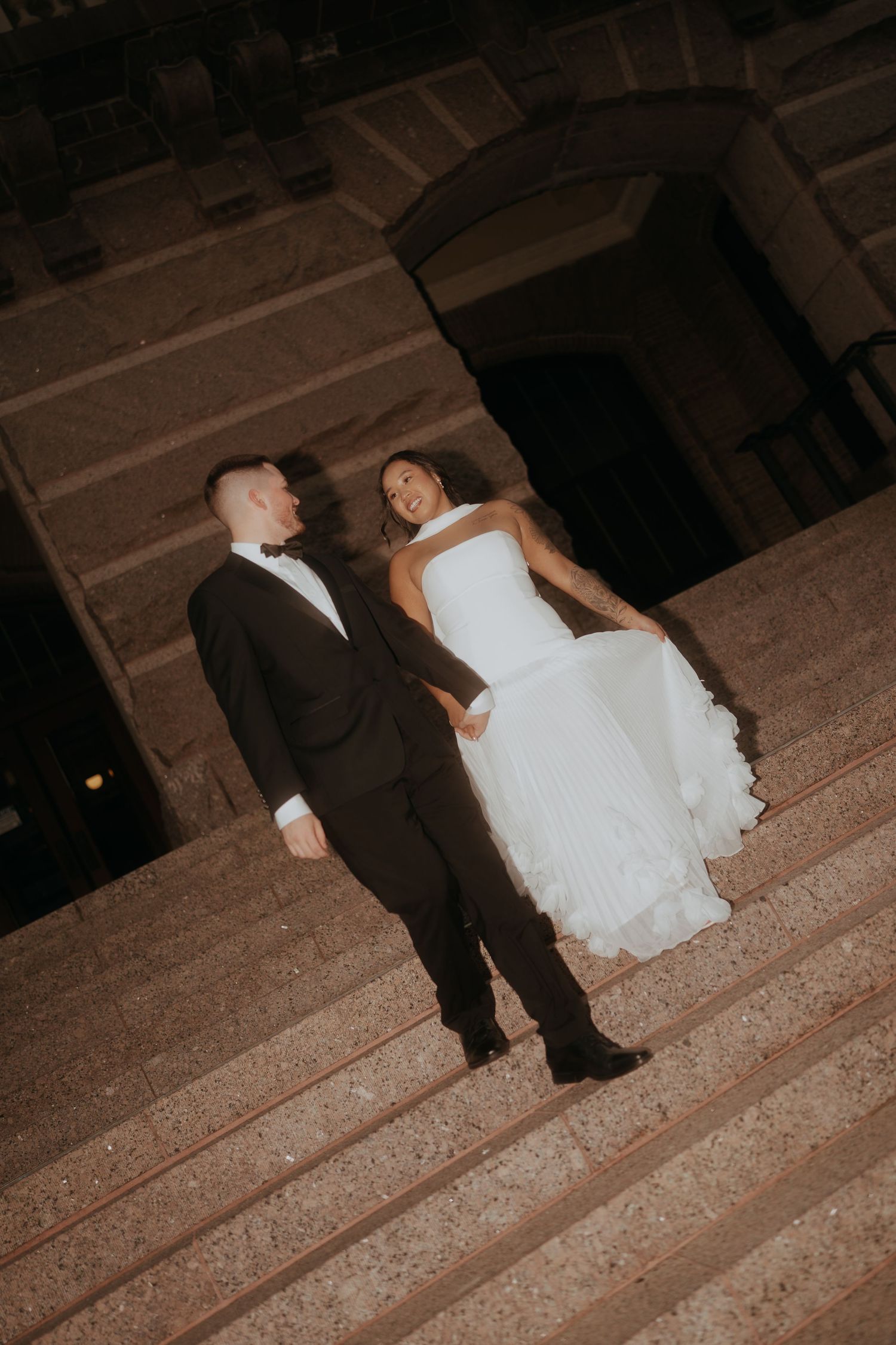 Bride and groom sharing a joyful moment on illuminated stone steps at night.