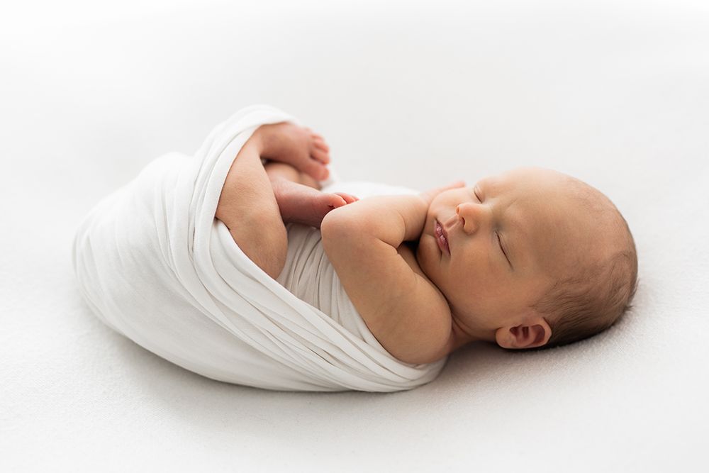 A newborn baby sleeping in a wrapped in a white fabric.