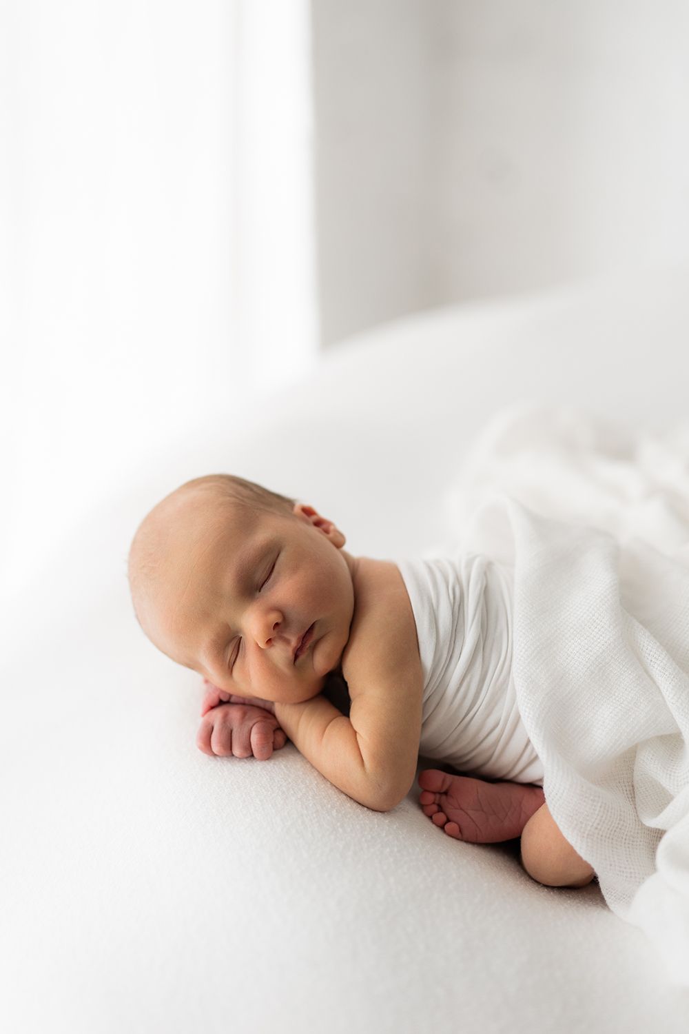 Newborn baby wrapped in a white fabric sleeping a on a bean bag.