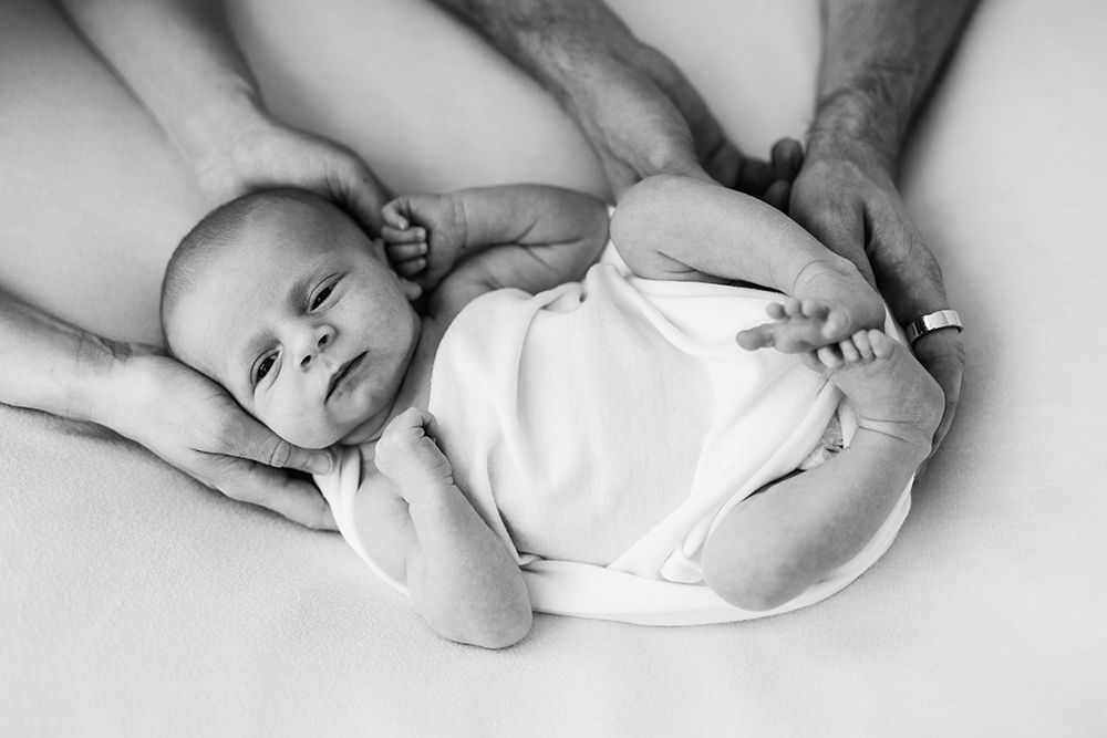 A newborn baby sleeping and parents hands holding baby's back. Black and white.