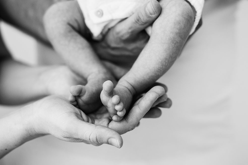 A parent hands holding a newborn baby feet. Black and white photo.