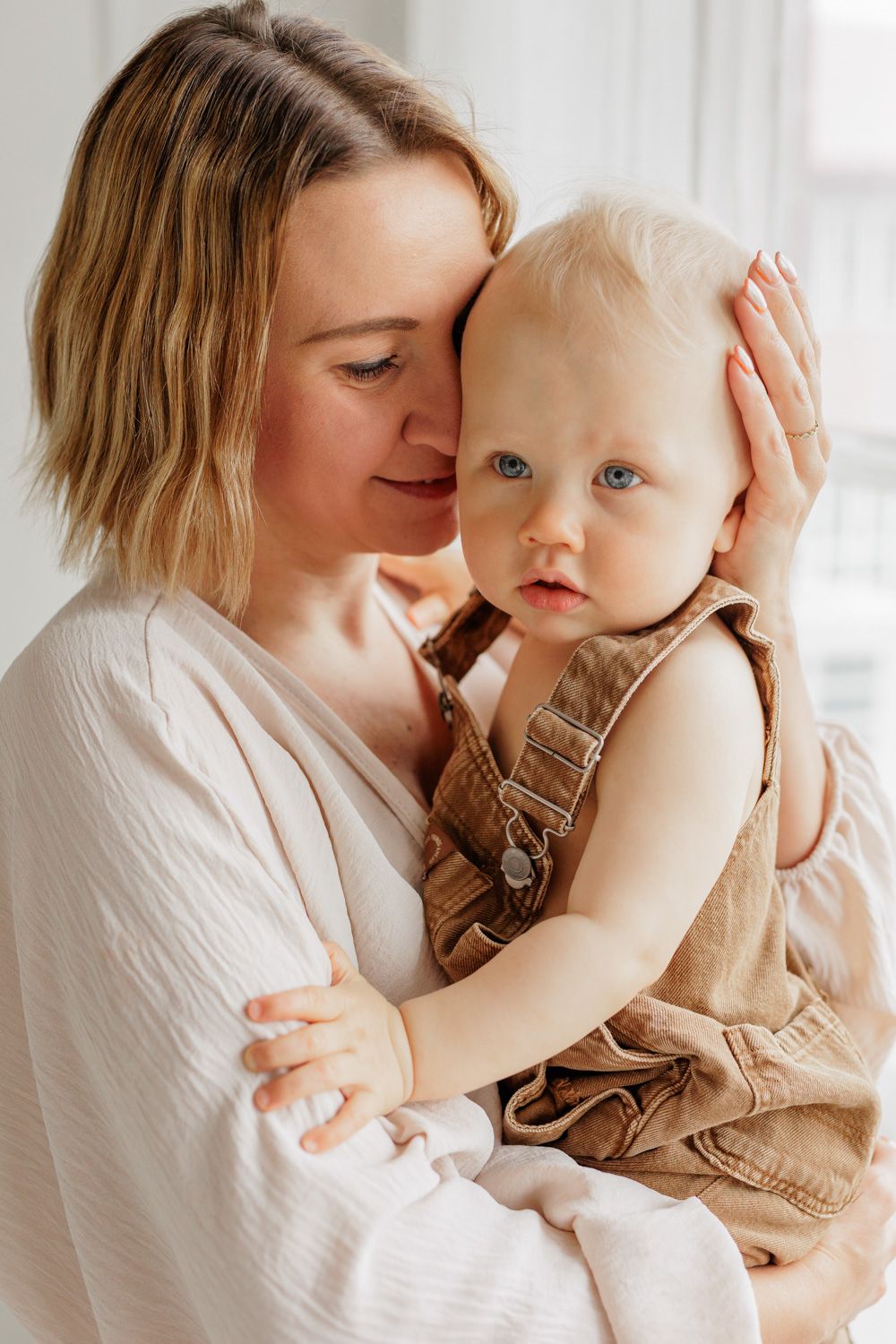 A mother holding her baby boy in front of a window.