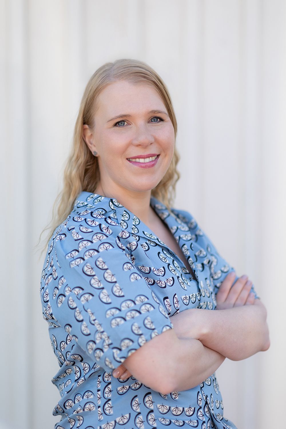 A blond hair woman smiling and looking in to a camera. Headshot. Outdoors.