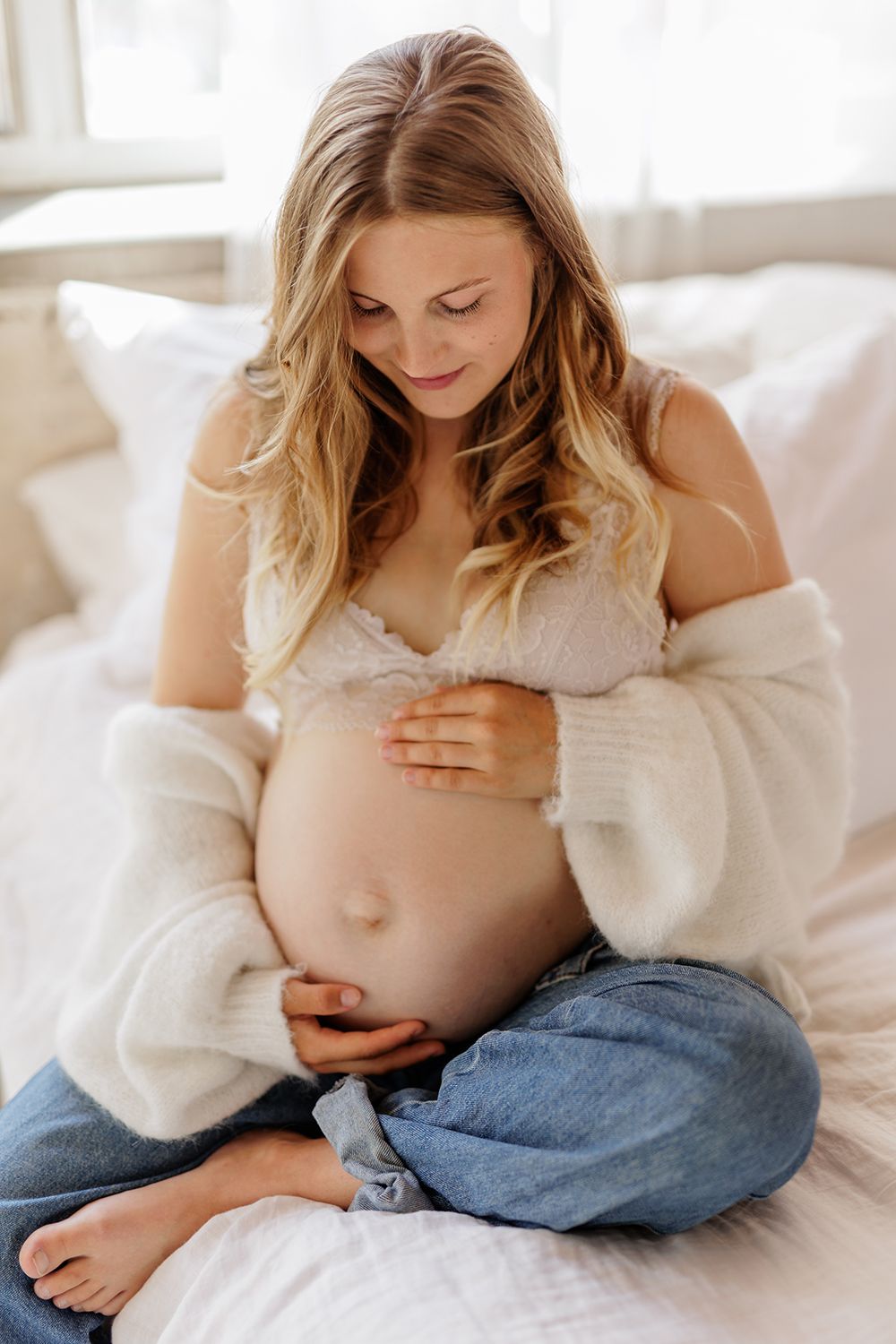 An expecting mother holding a baby bump and sitting on a bed.