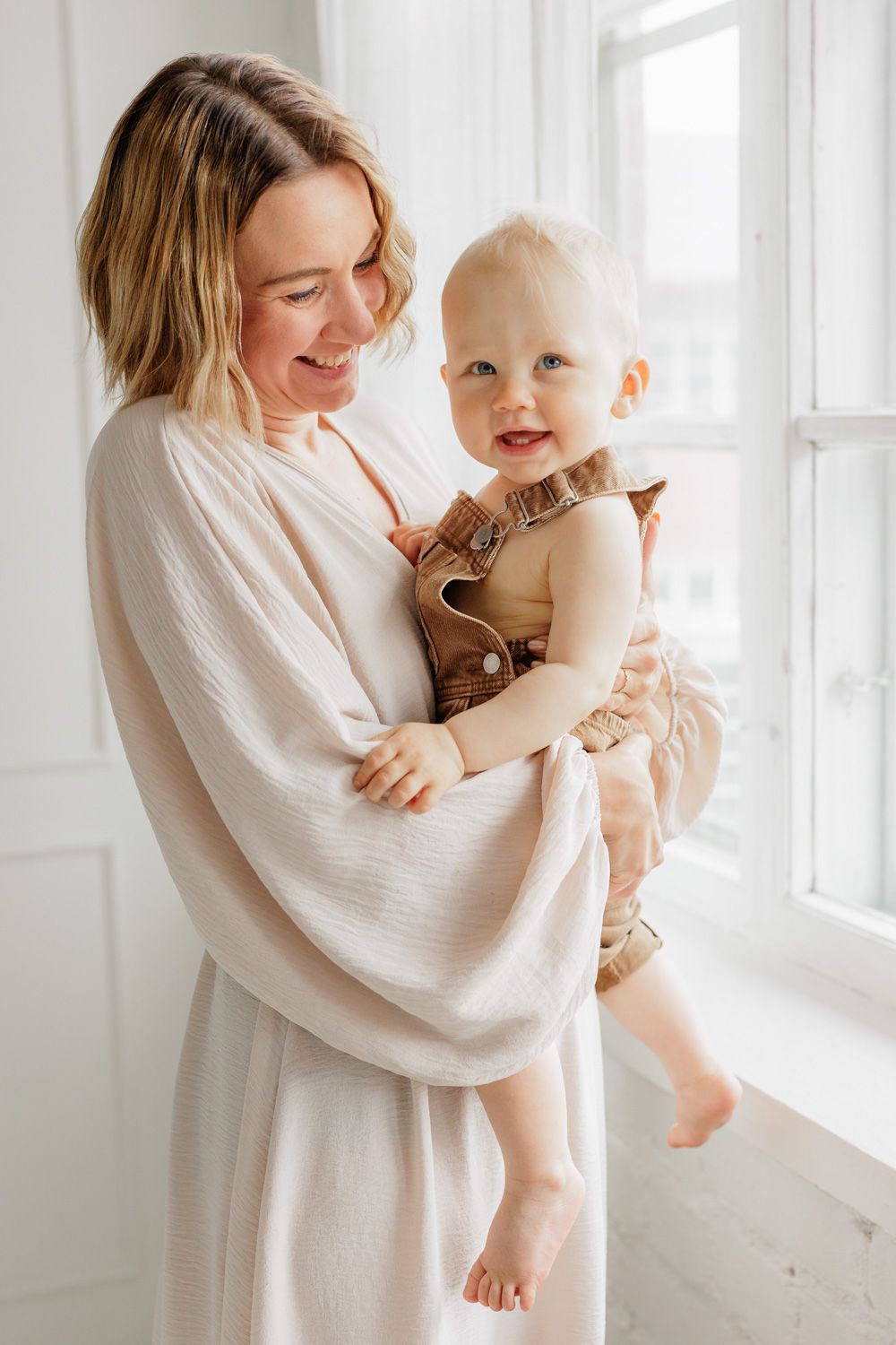 A mother holding her baby boy in front of a window.