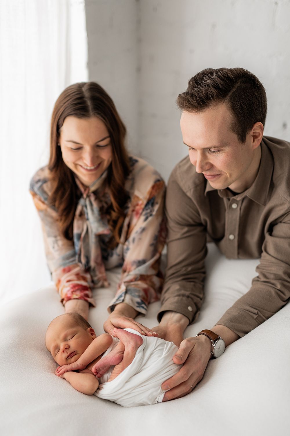 A mother and a father holding a newborn sleeping on a white bean bag.