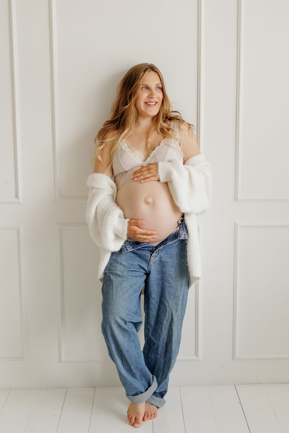 An expecting mother holding a baby bump and leaning on a wall.
