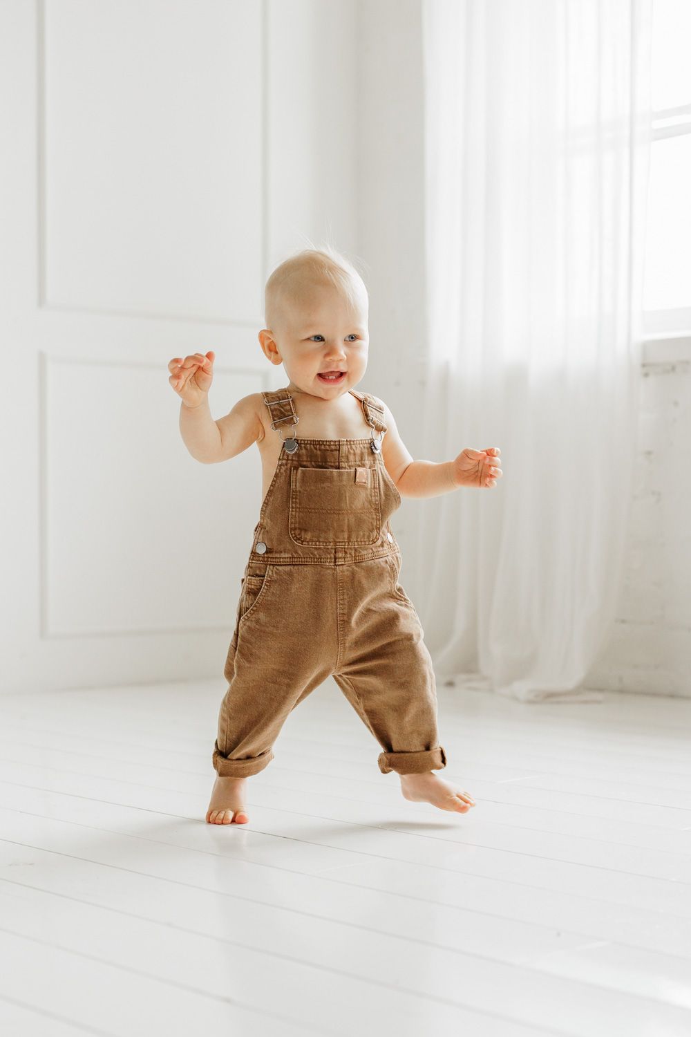 A baby boy smiling and running in a white room.