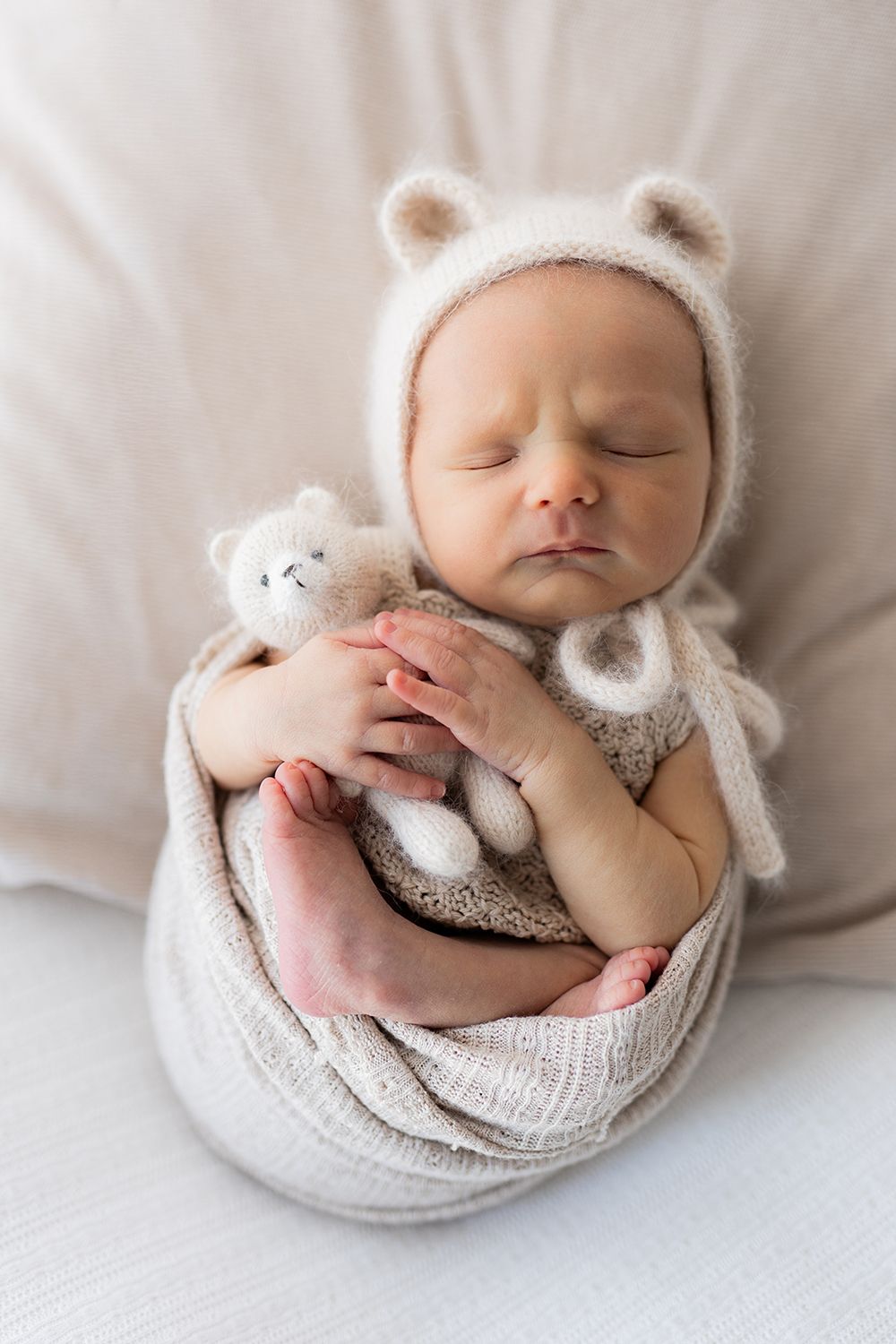 Newborn baby sleeping on a pillow holding a small teddy bear.