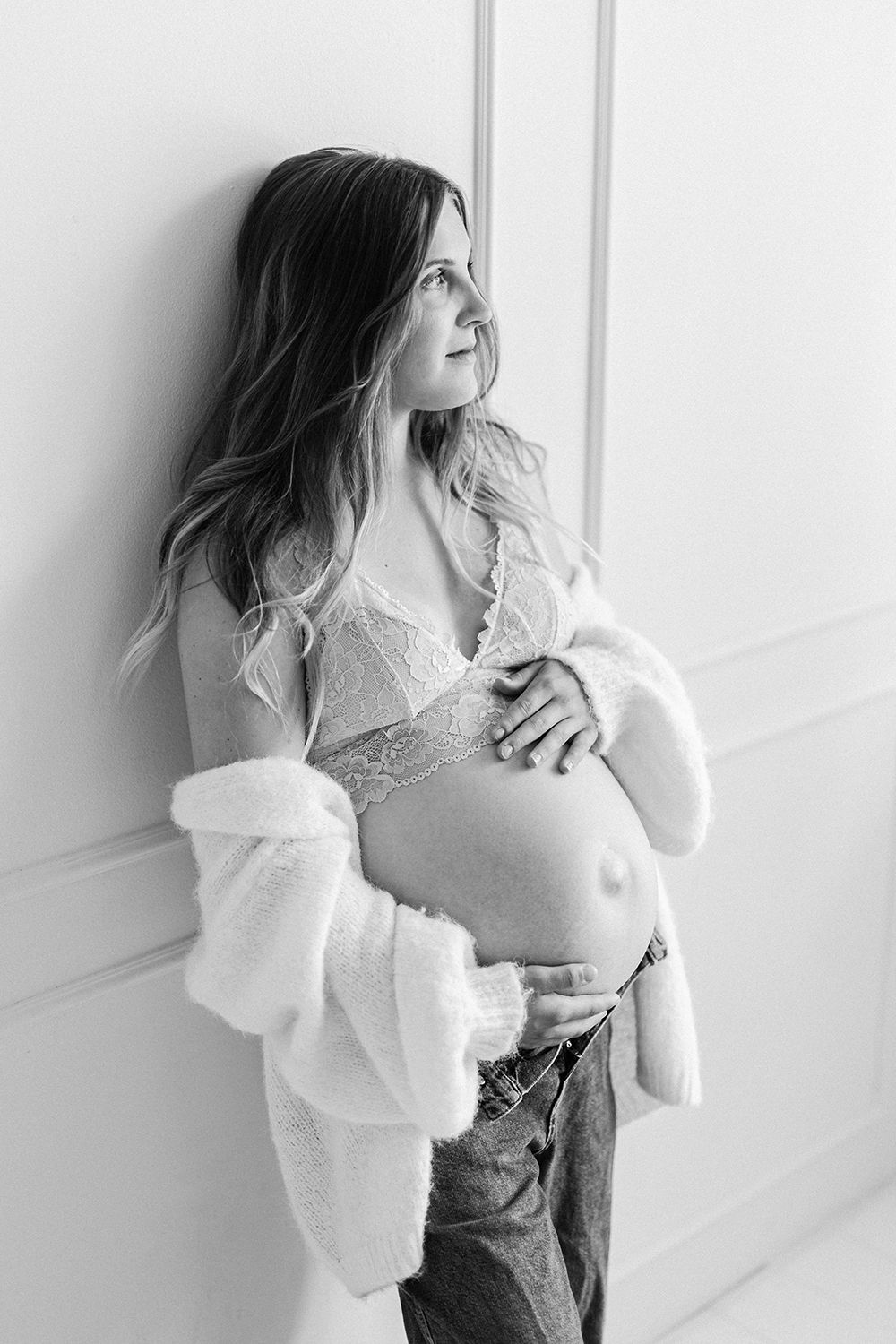 An expecting mother holding a baby bump and leaning on a wall.