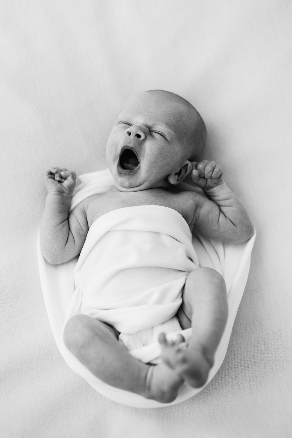 A newborn baby yawning on a white surface. Back and white.