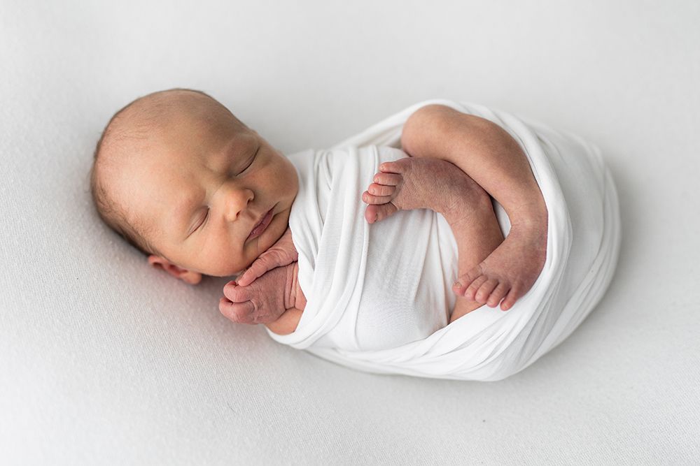 Newborn baby wrapped in a white fabric sleeping a on a bean bag.