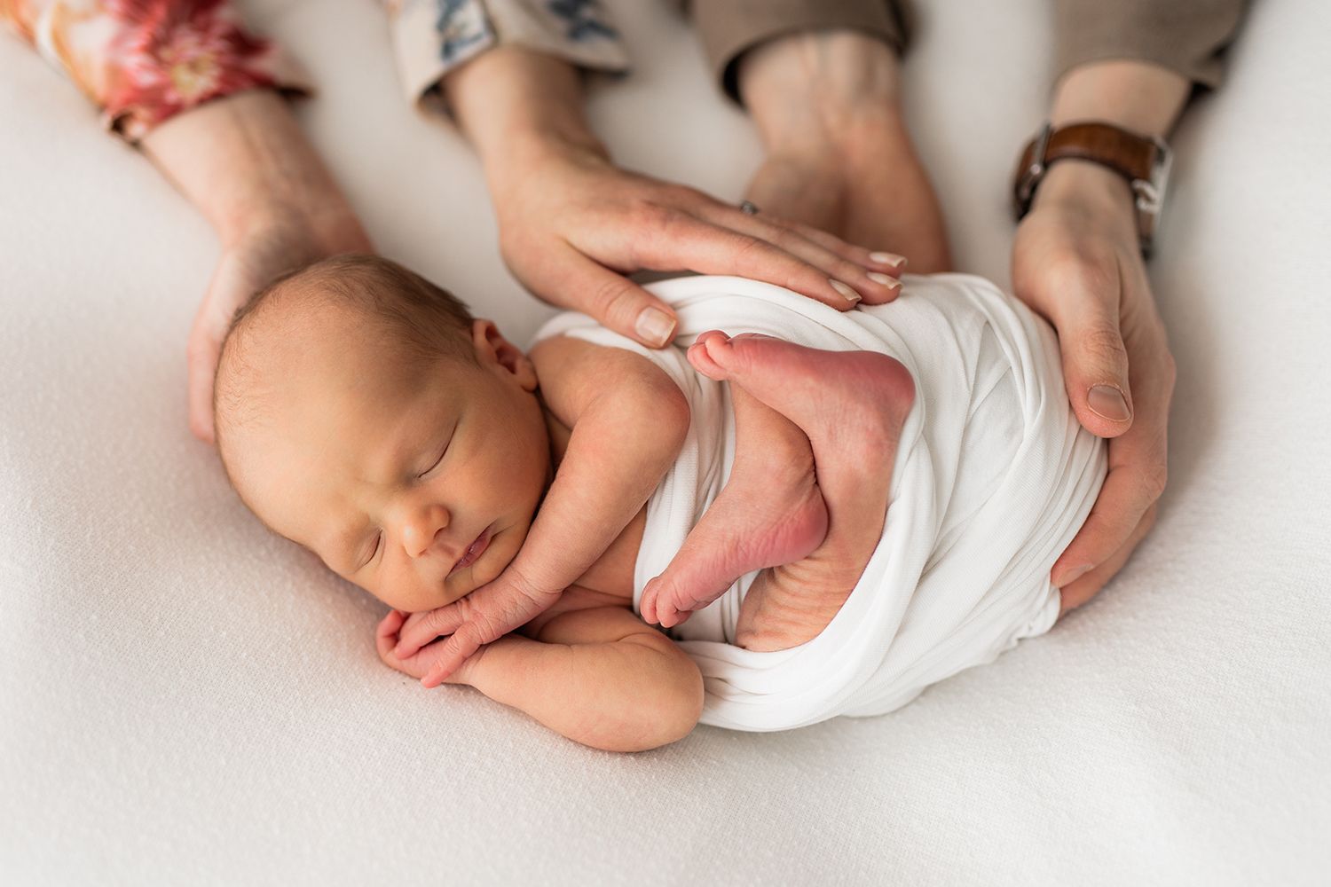 A newborn baby sleeping and parents hands holding baby's back.
