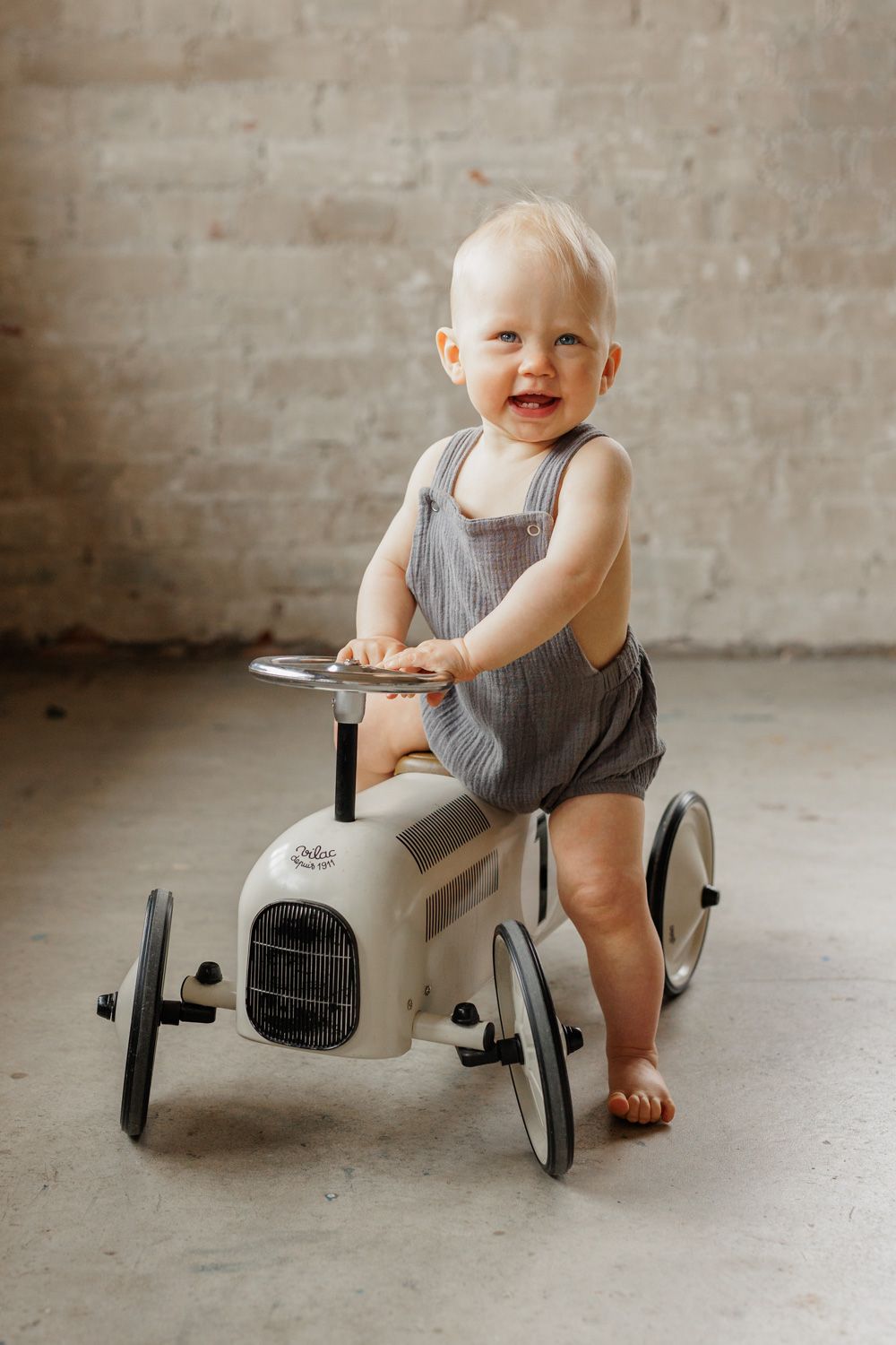 A baby boy sitting on a moped and looks at a camera and smiles.