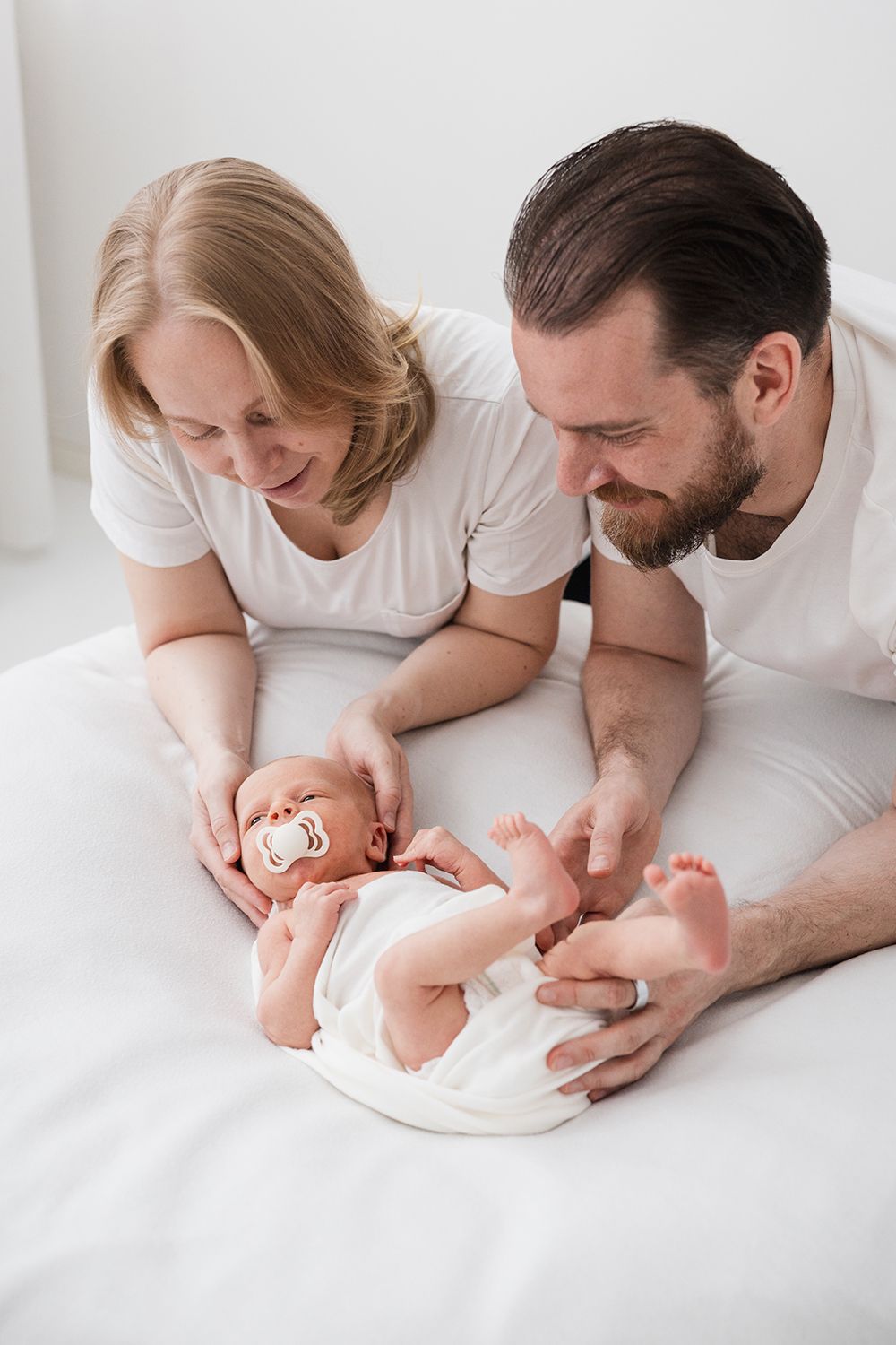 Mother and a father holding a newborn baby who is laying on a white bean bag.