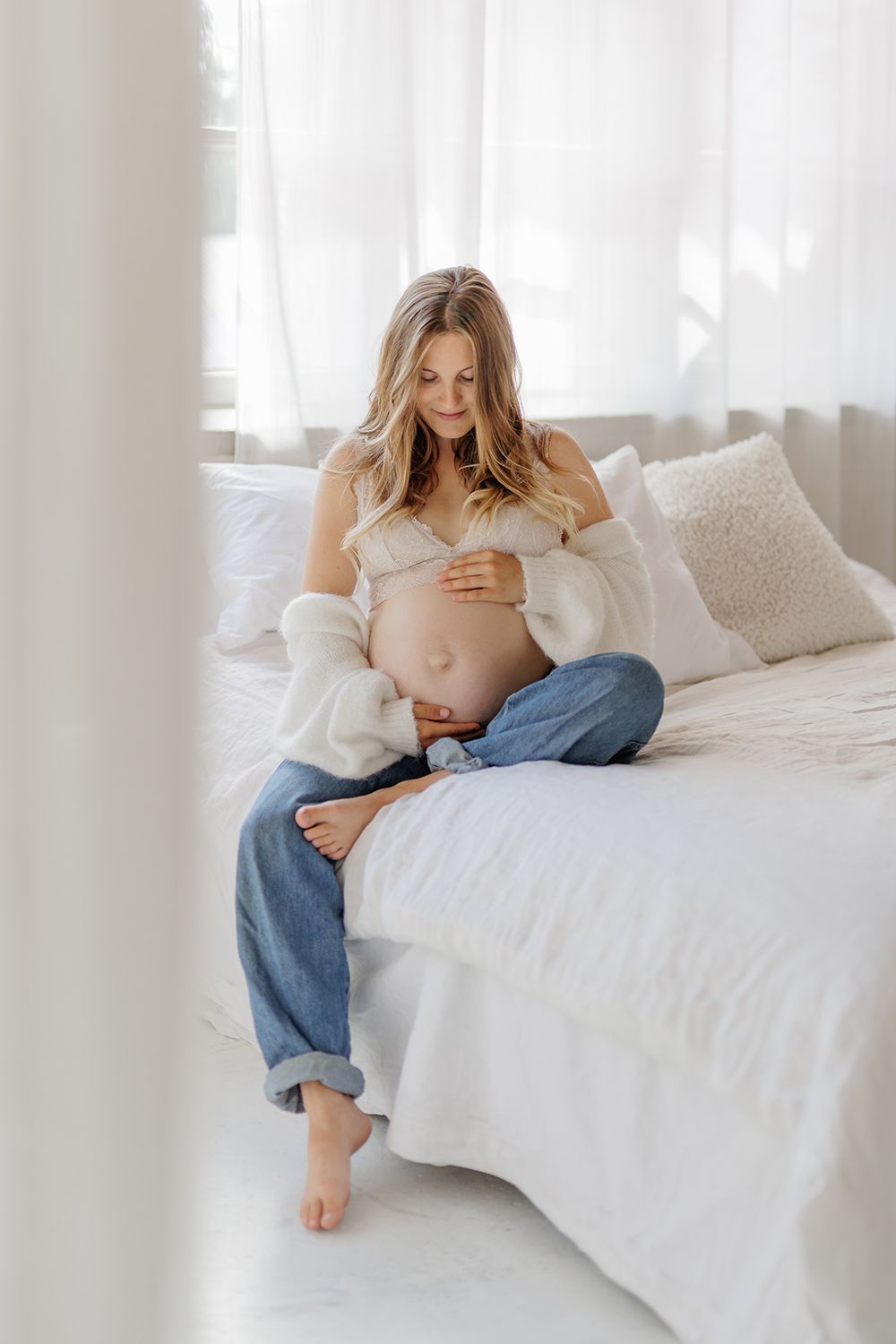 An expecting mother holding a baby bump and sitting on a bed.