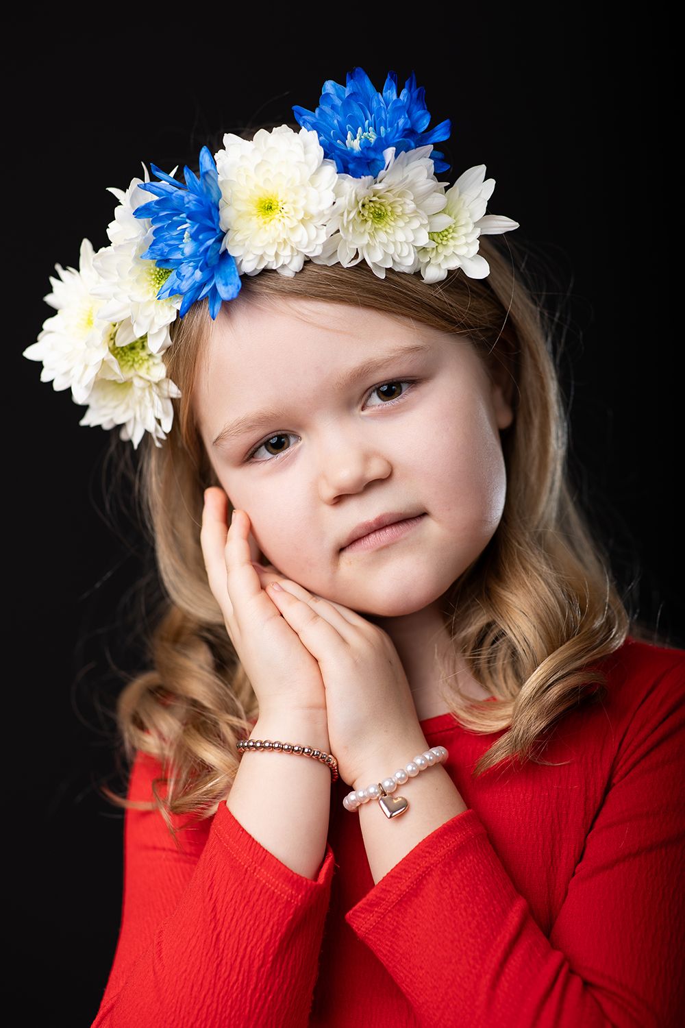A girl in a red shirt with flower in her hair posing in a photo studio black background.