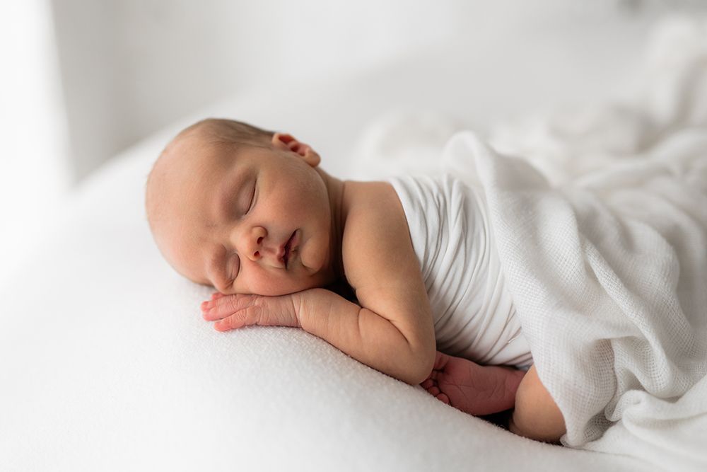 Newborn baby wrapped in a white fabric sleeping a on a bean bag.