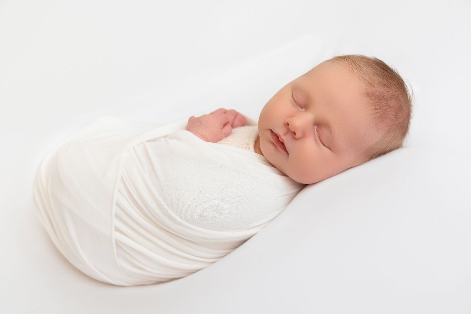 Sleeping newborn baby swaddled in white wrap lying on white background.