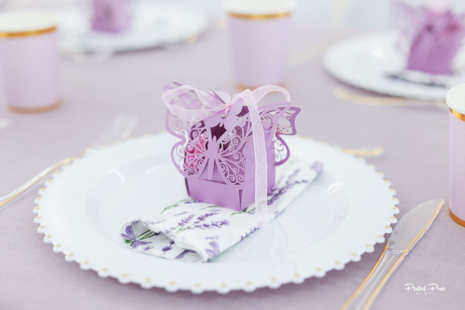 Elegant lavender wedding table setting with decorative laser-cut butterfly favor box on white charger plate.