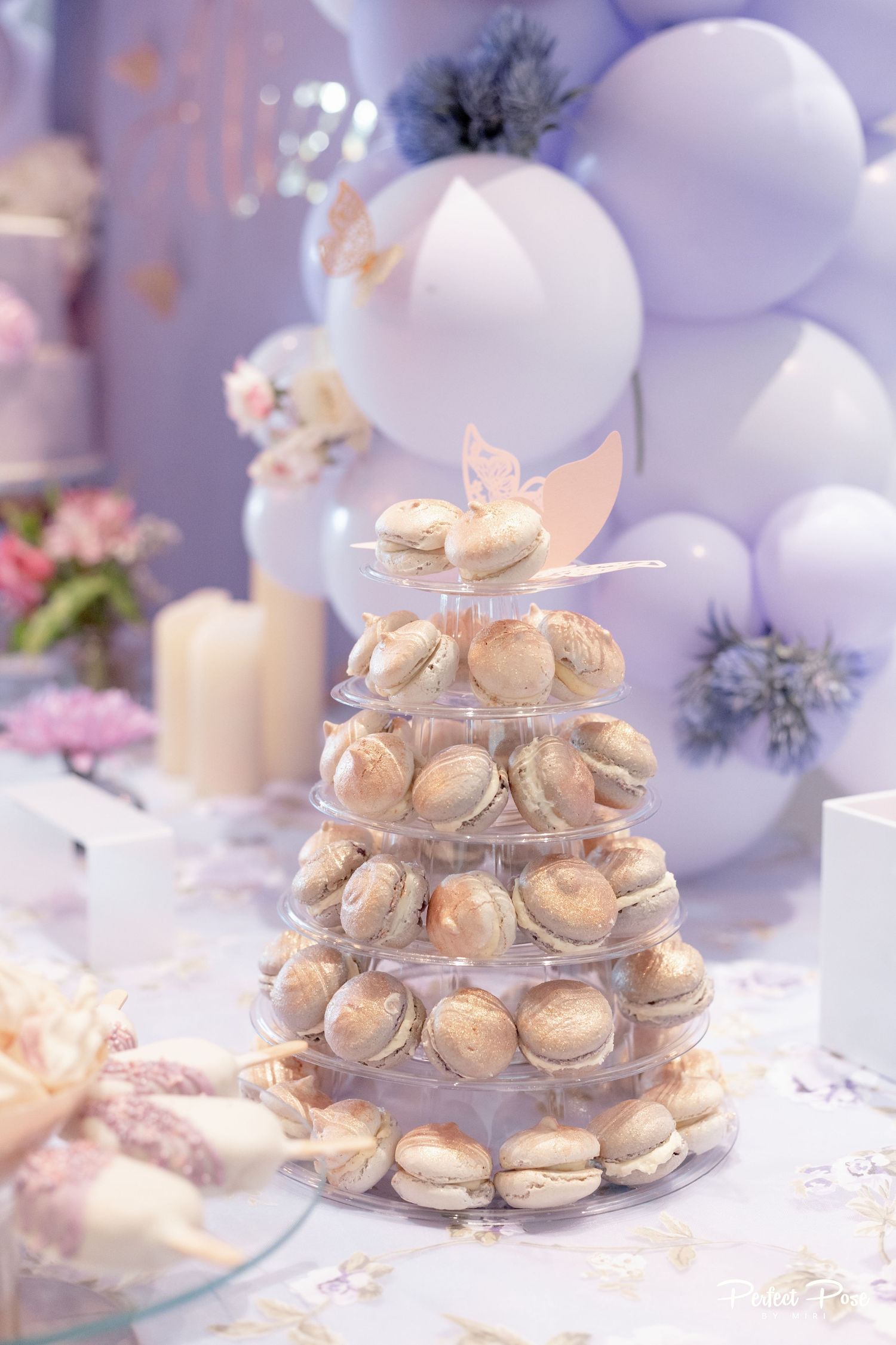 Elegant macaron tower display with butterfly topper at a pastel purple party with balloon backdrop.