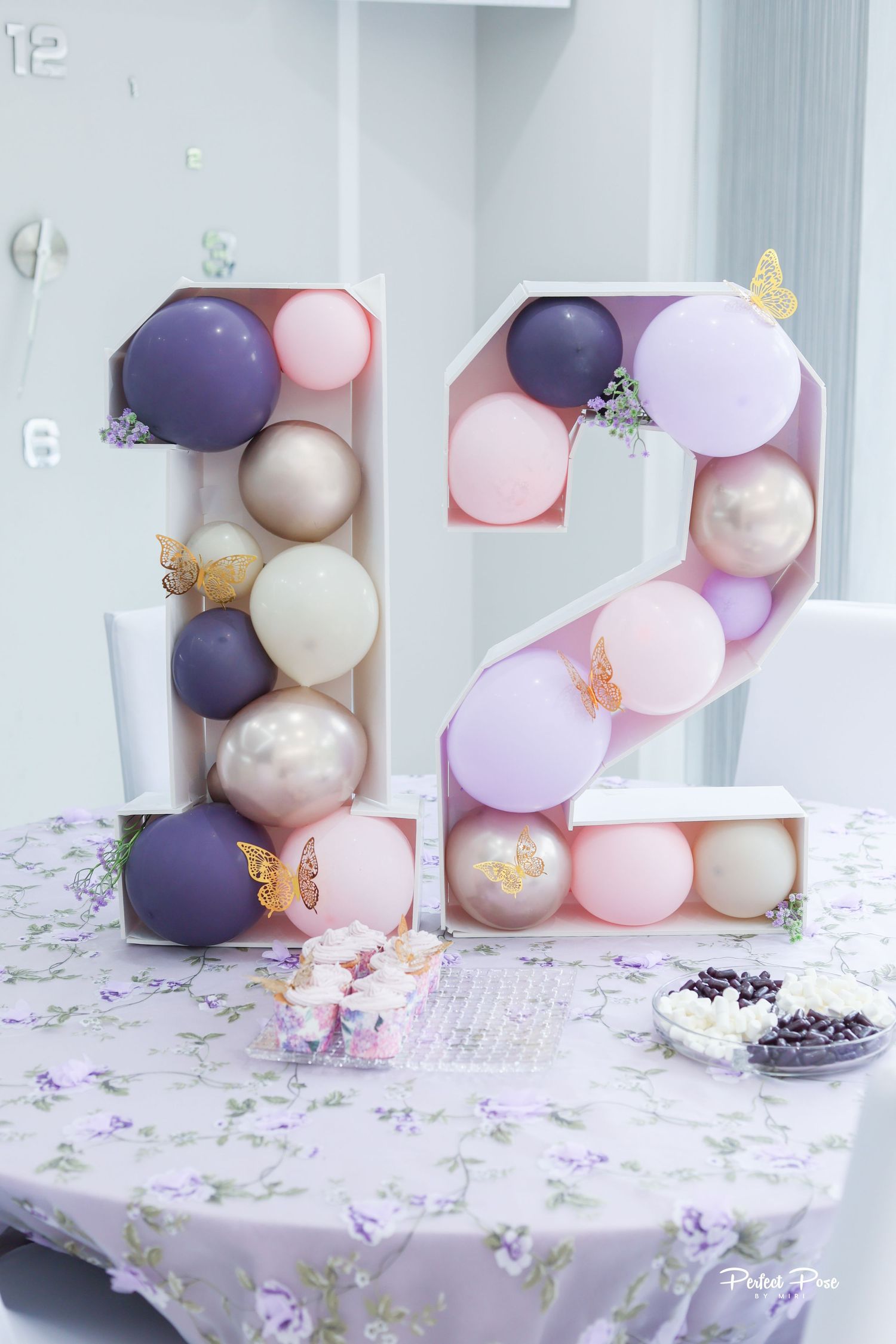 Large number 12 balloon mosaic display with purple, pink, and gold balloons on a floral table for a birthday party.
