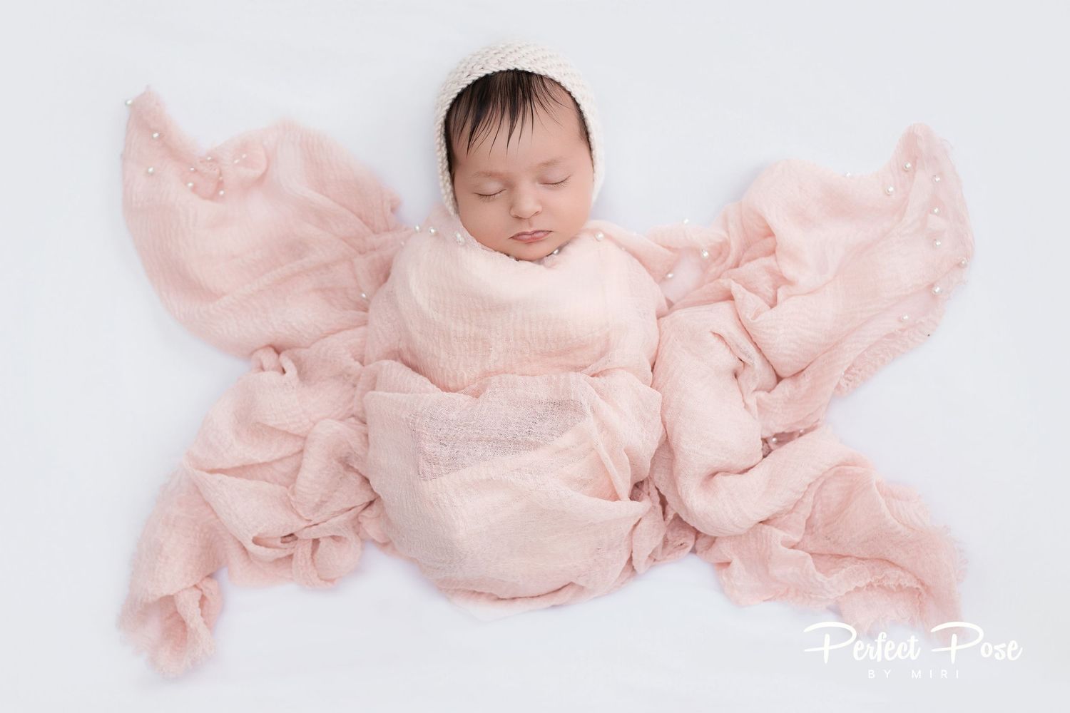 Newborn baby sleeping peacefully wrapped in soft pink fabric on white background, professional newborn photography.