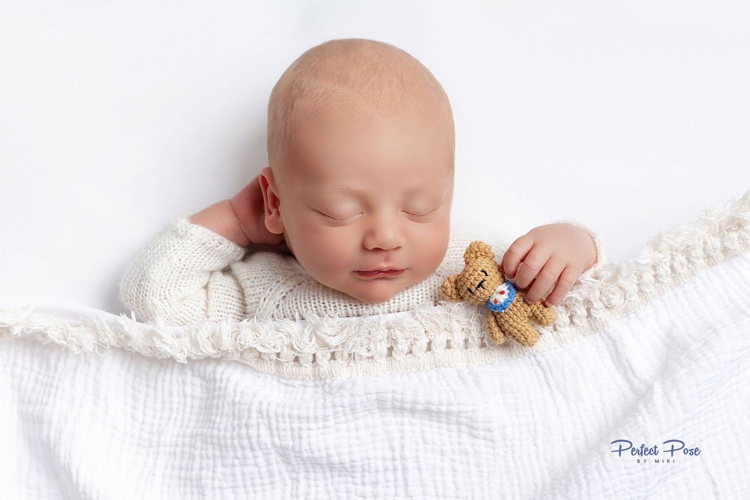 Peaceful newborn baby sleeping wrapped in white blanket holding a small knitted teddy bear.