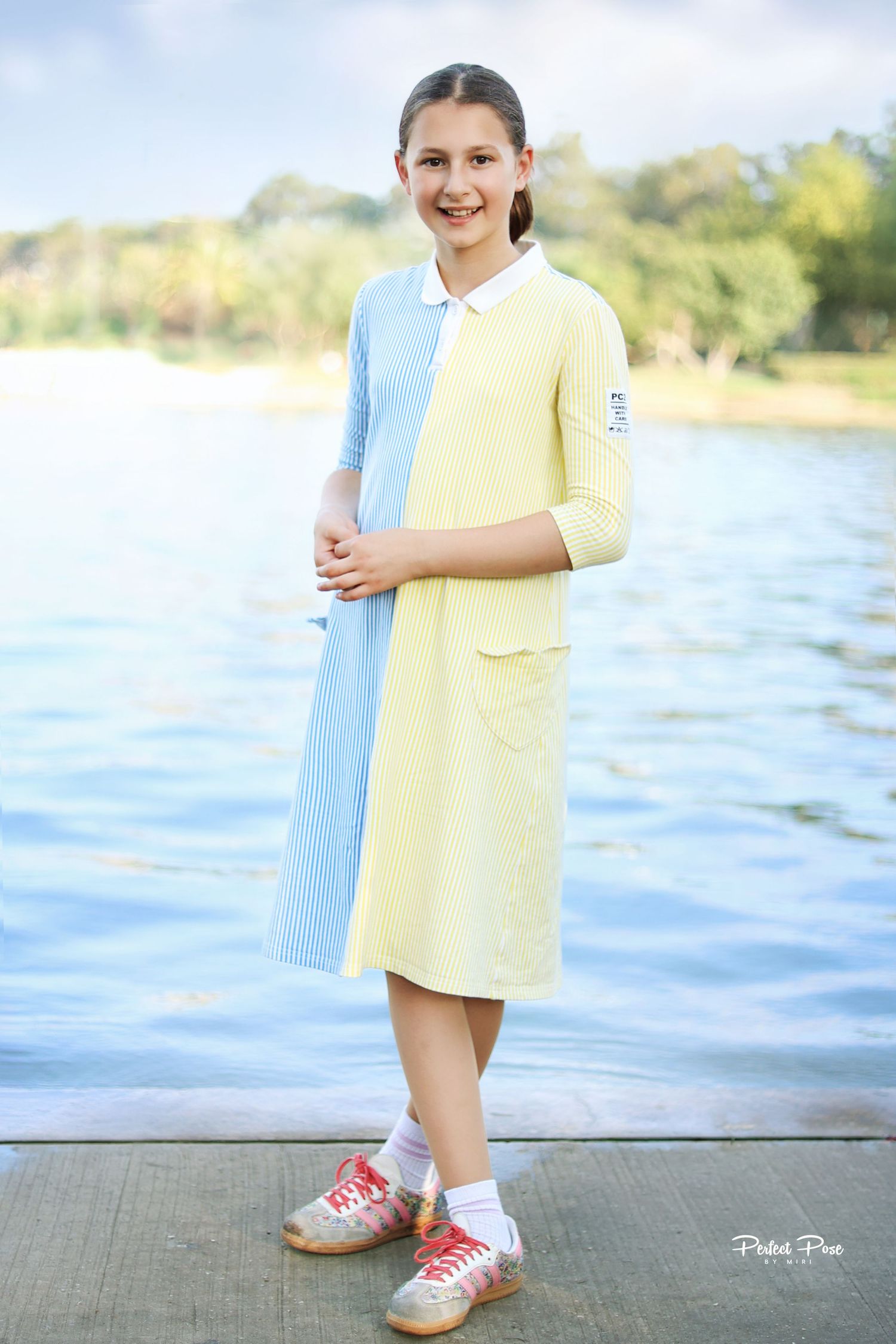 Girl wearing a two-tone blue and yellow polo dress with 3/4 sleeves, standing near a lake wearing pink sneakers.