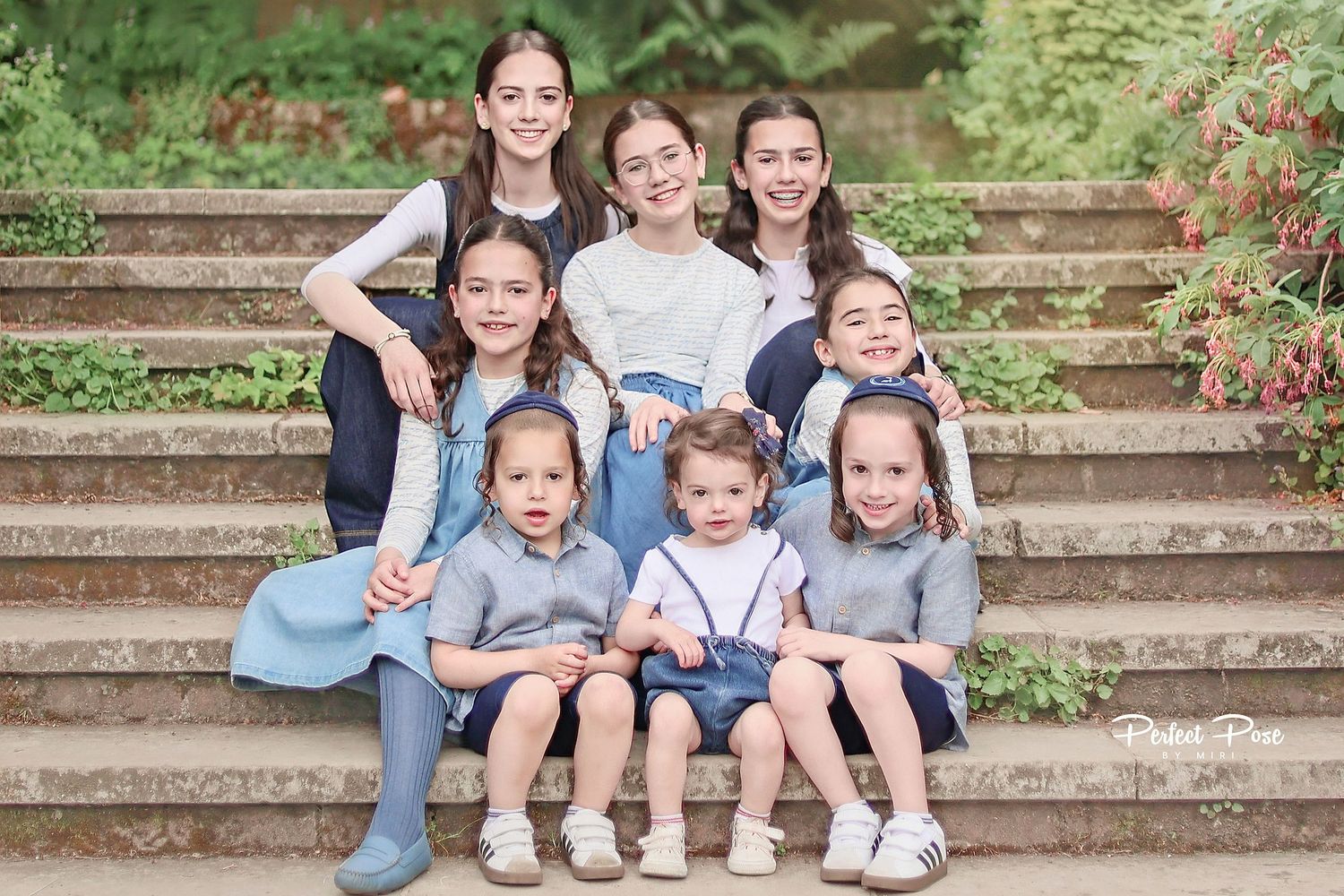 Group of eight children posing on stone steps outdoors, dressed in coordinating blue and white outfits for a family portrait.