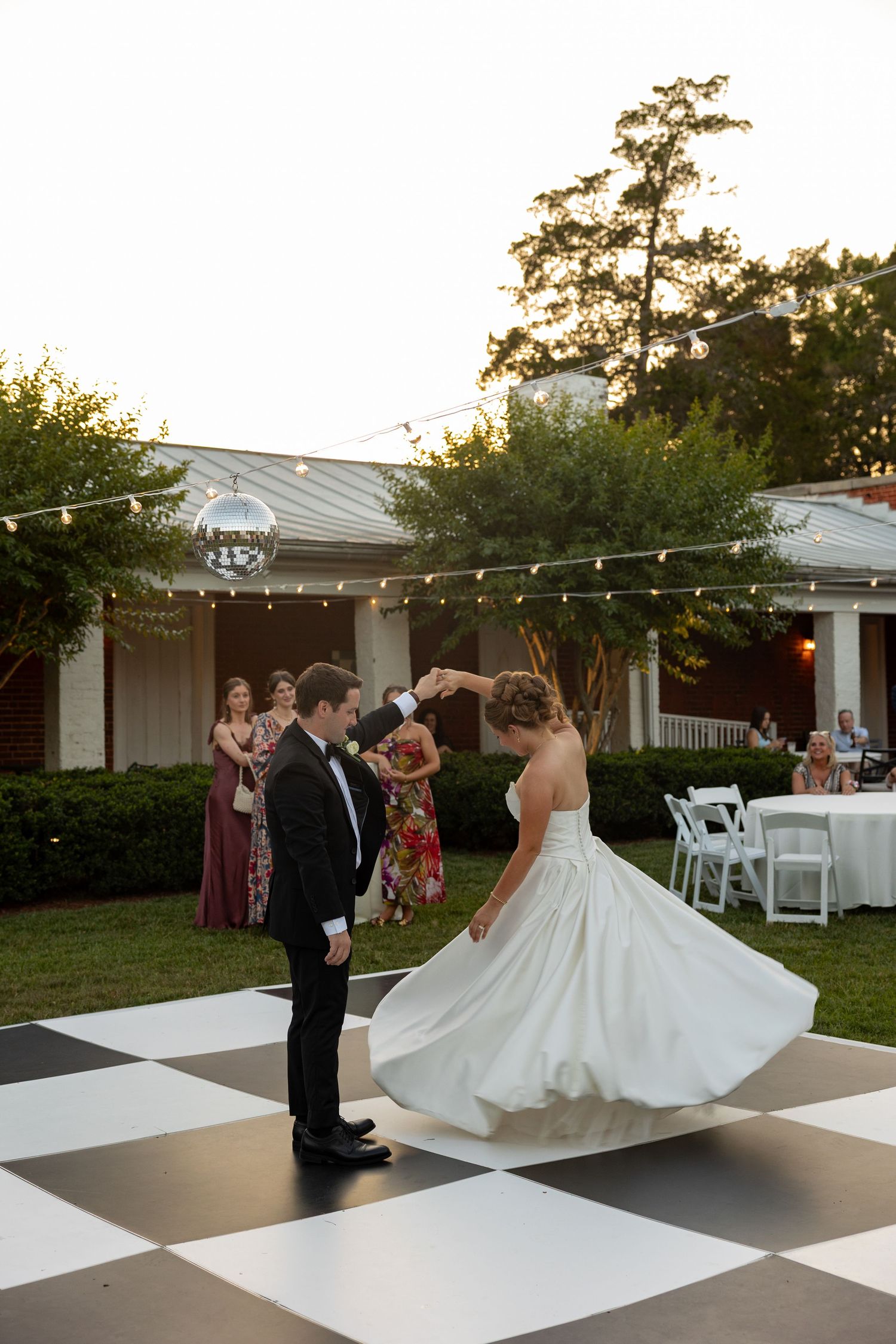 Bride and groom dancing at dusk on a black and white checker floor.