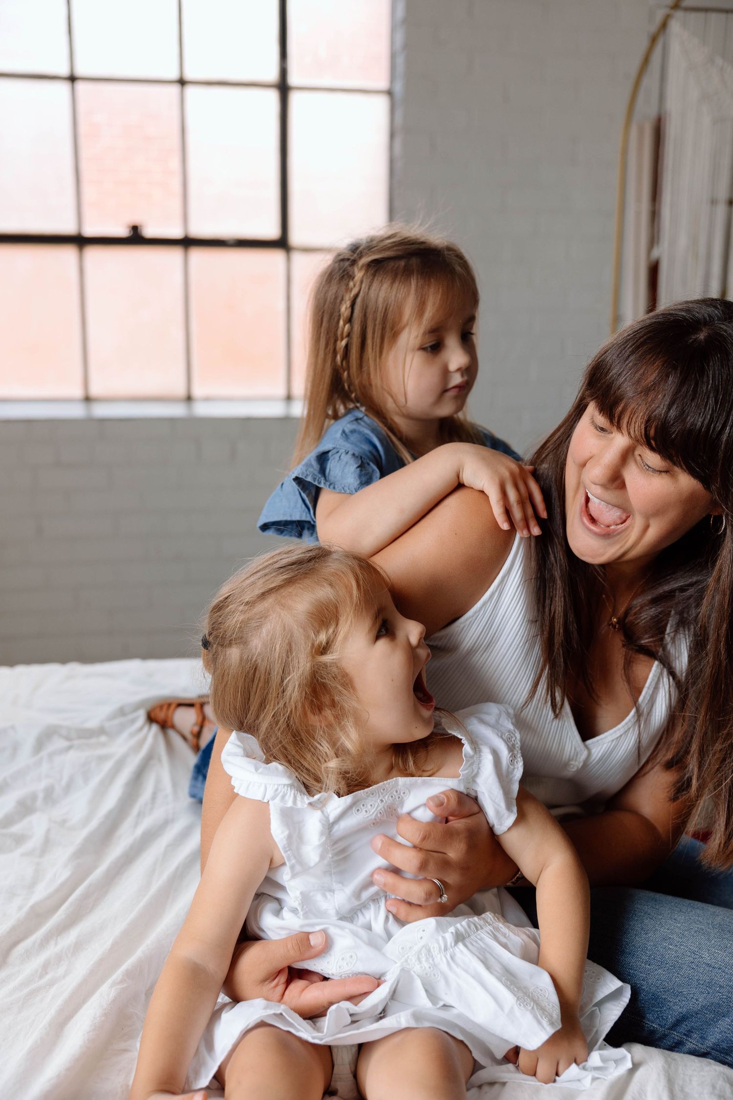 mom and two daughters playing on a bed