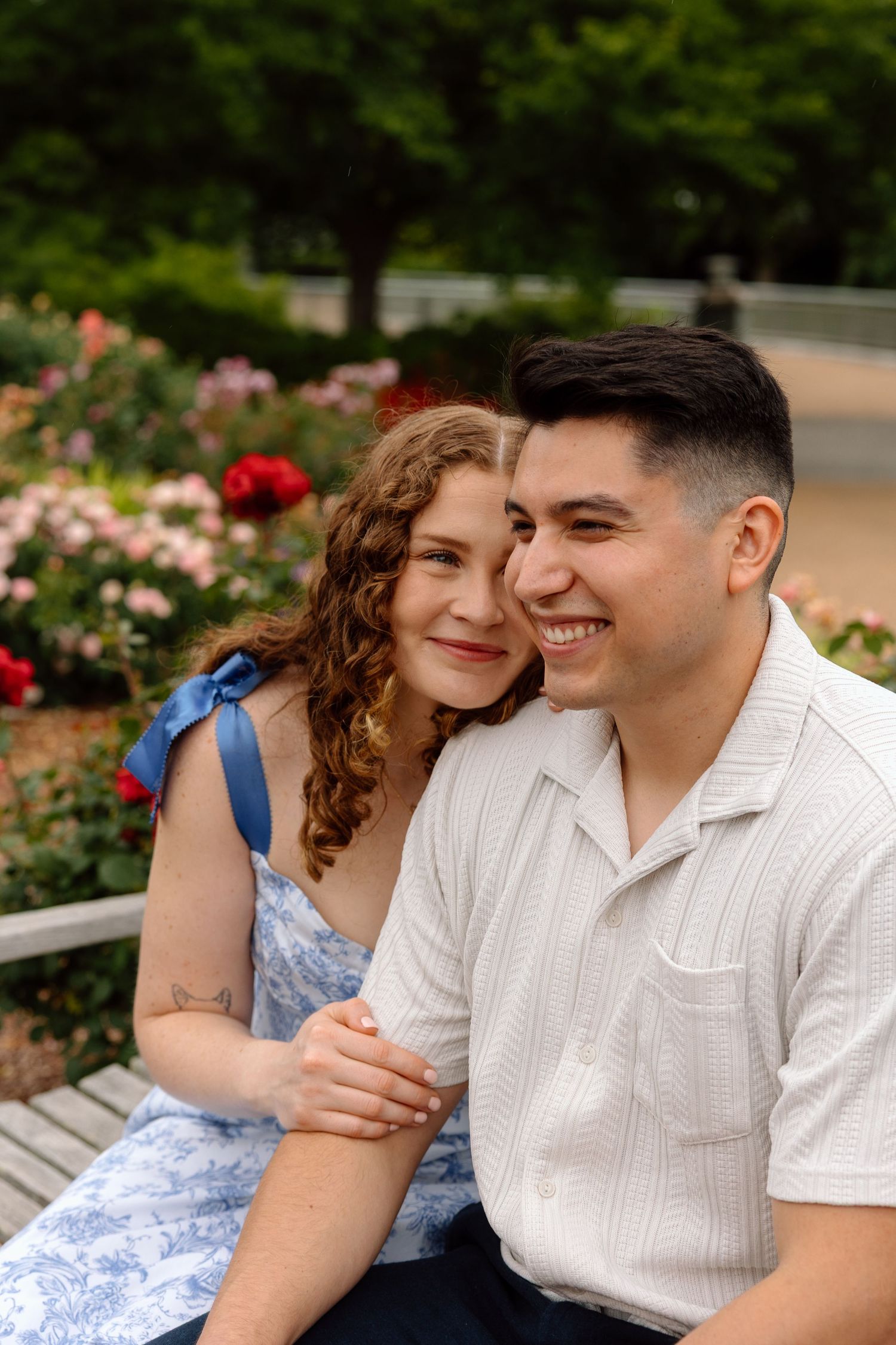 Man and woman sitting on bench, woman smiling at man as he looks off into distance.