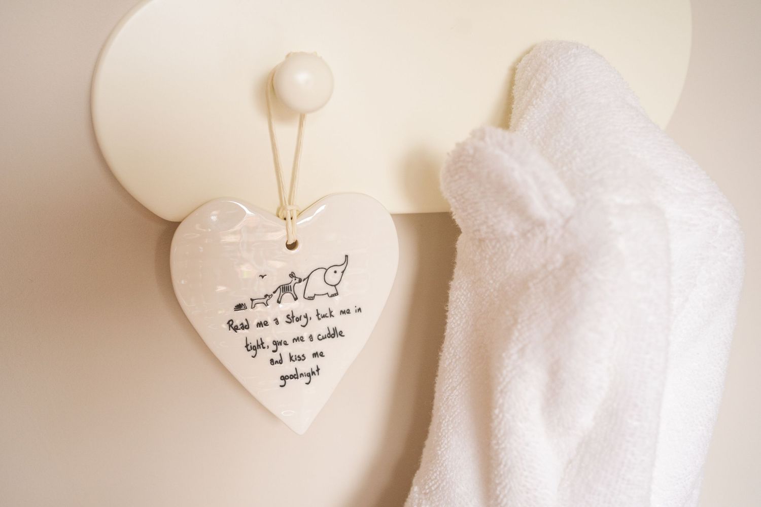 White ceramic heart keepsake plaque with handwritten poem hanging on wall hook beside fluffy white baby towel.
