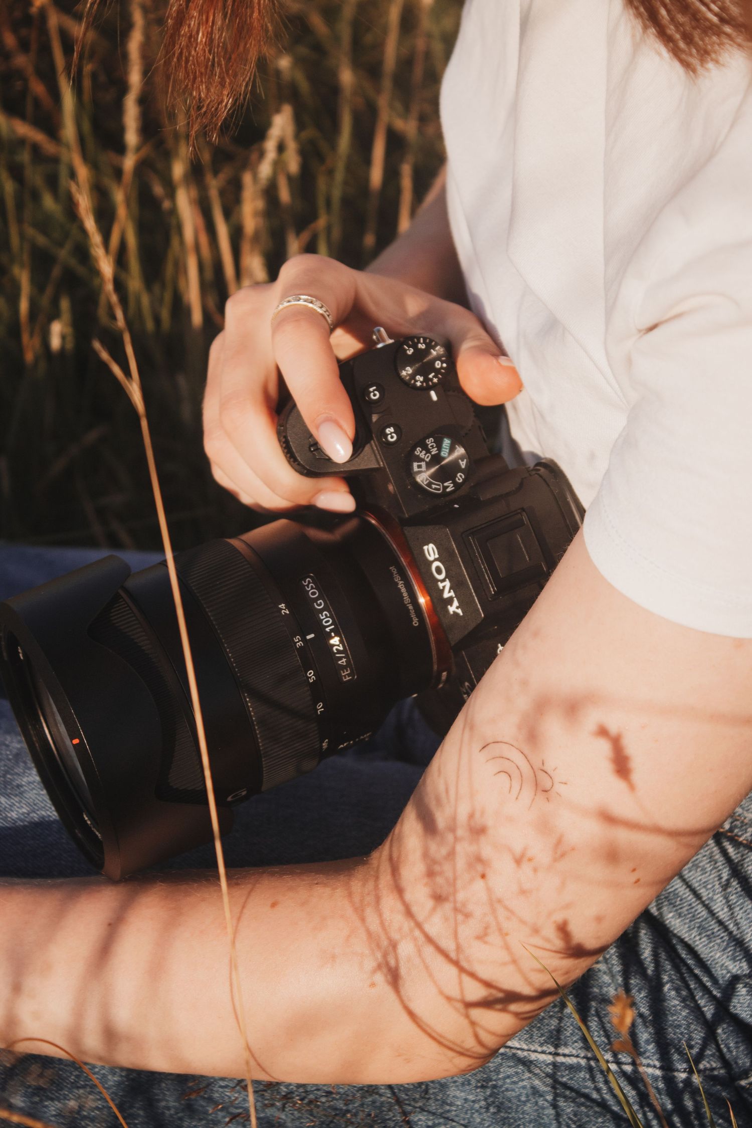 Close-up of a Sony mirrorless camera held by a woman with rings and tattoos.